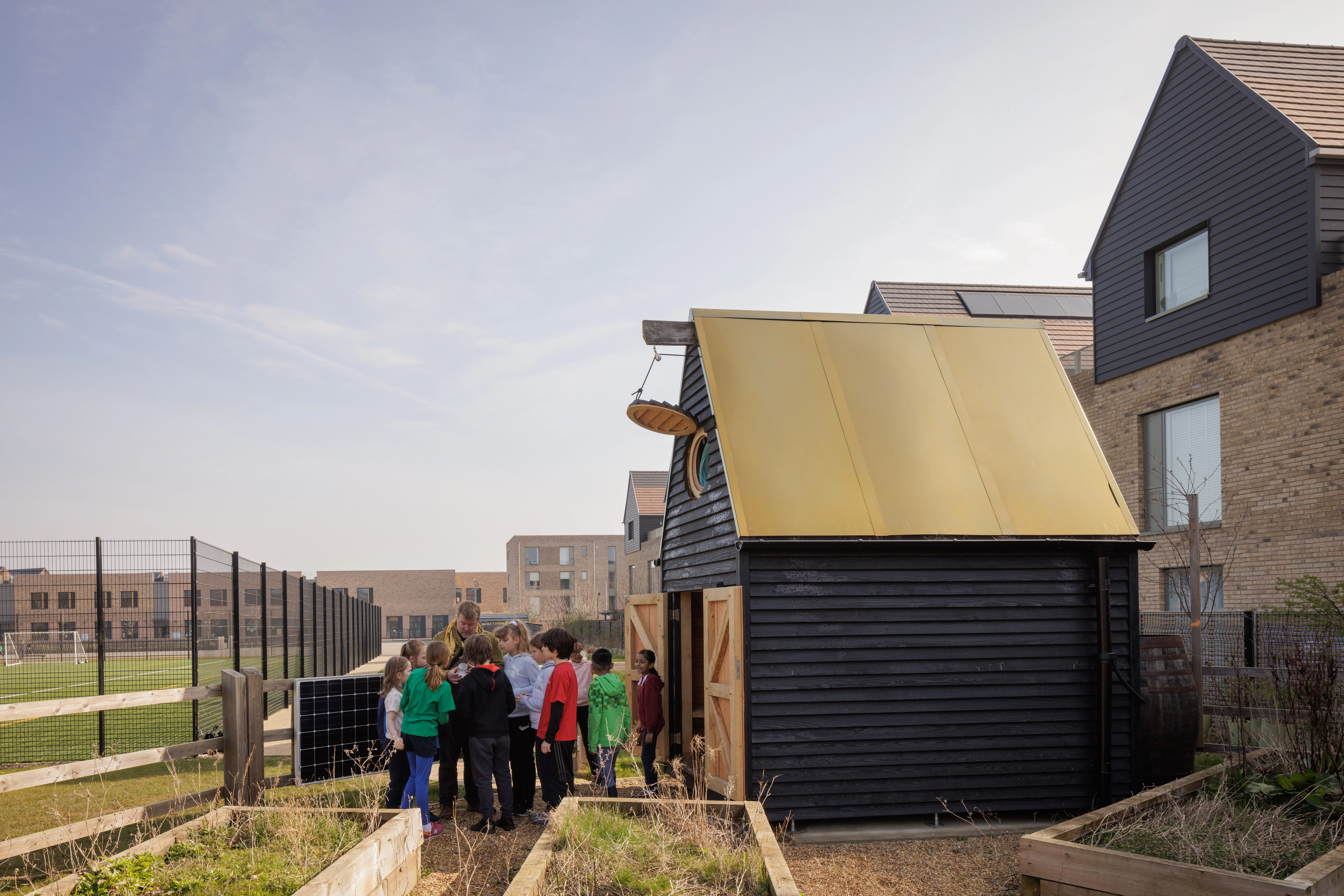 Children outside a black clad oak framed cabin with reflective steel roof