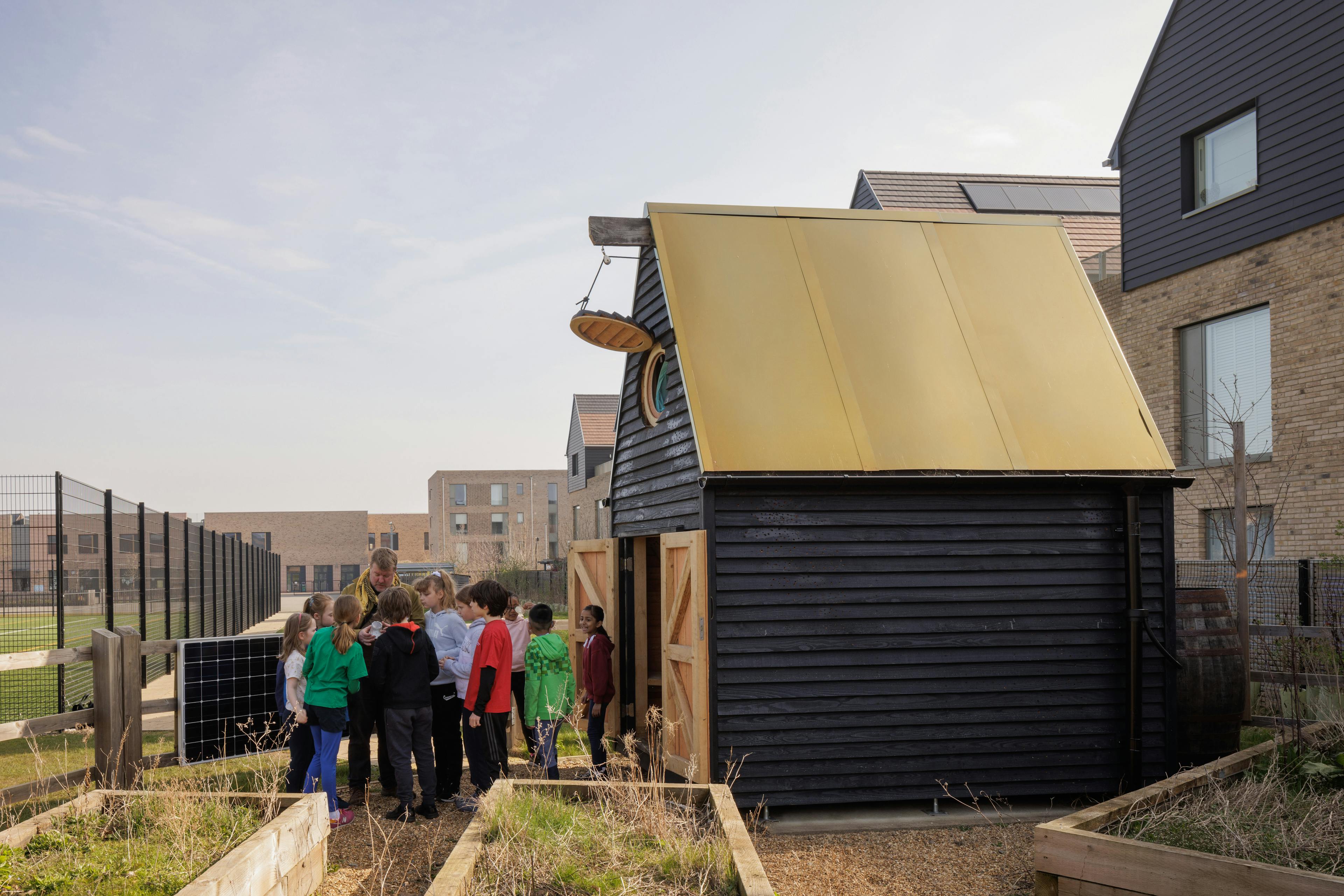 Children outside a black clad oak framed cabin with reflective steel roof