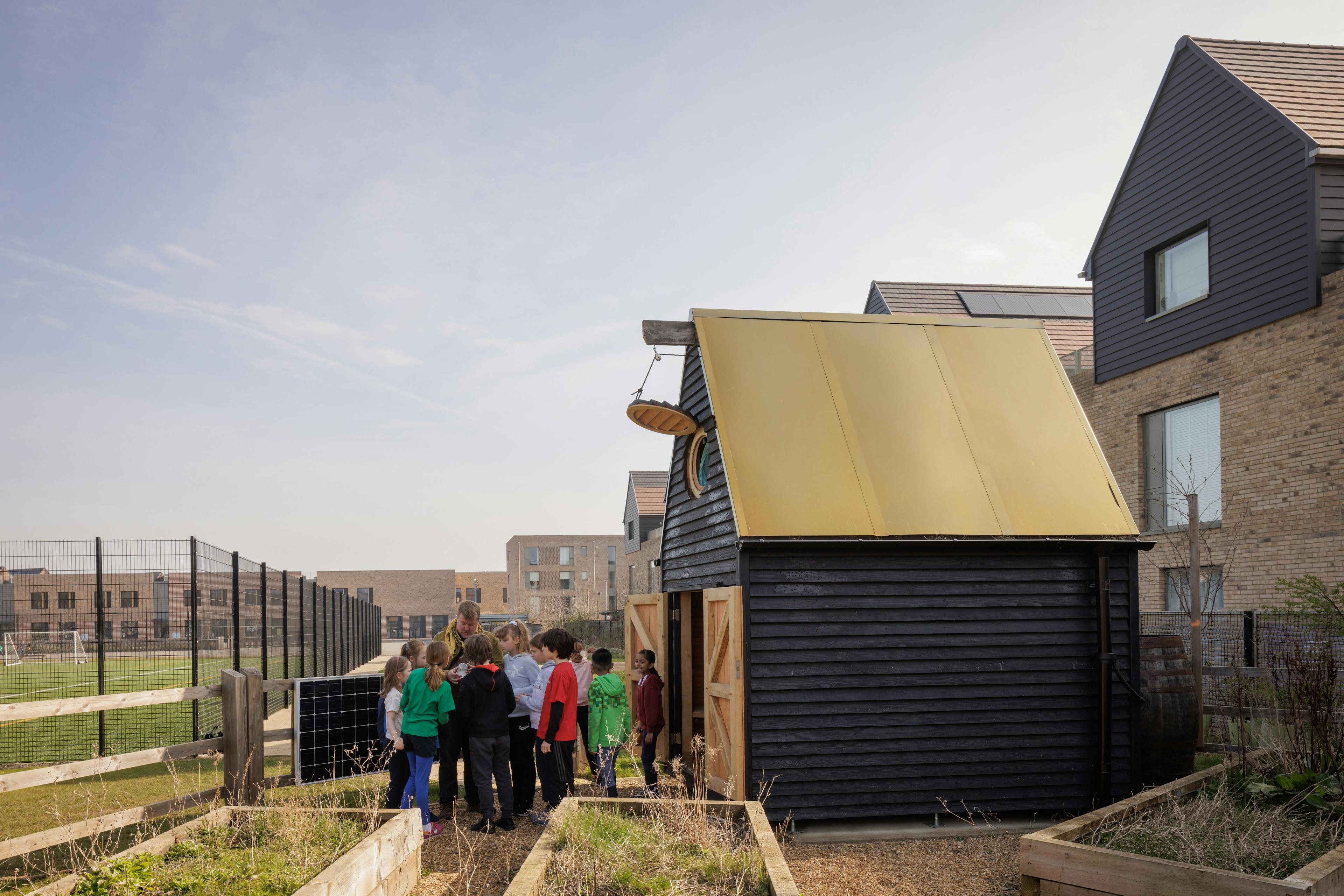 Children outside a black clad oak framed cabin with reflective steel roof