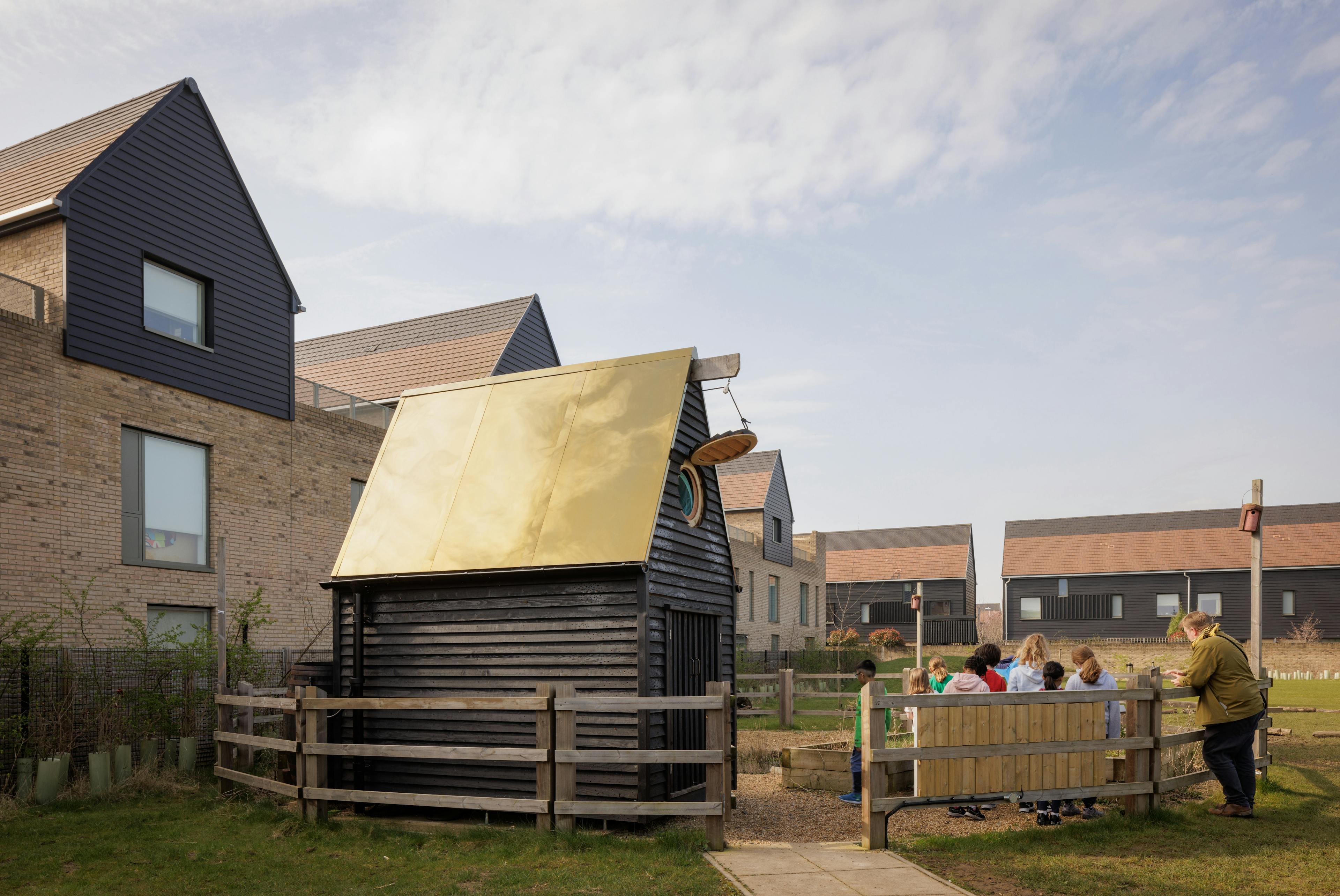Children outside a black clad oak framed cabin with reflective steel roof