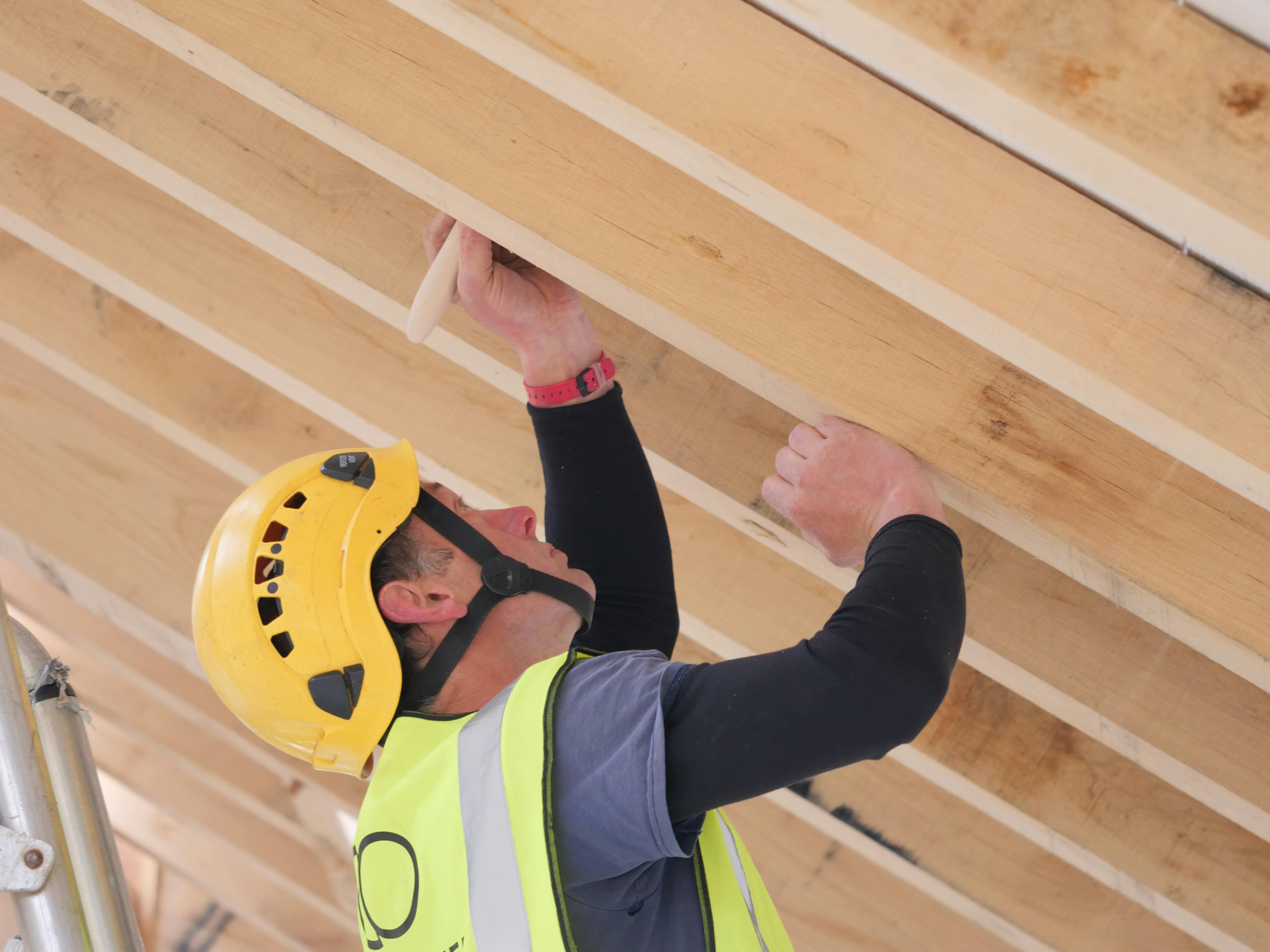 A carpenter installing white painted roof boarding to an oak frame