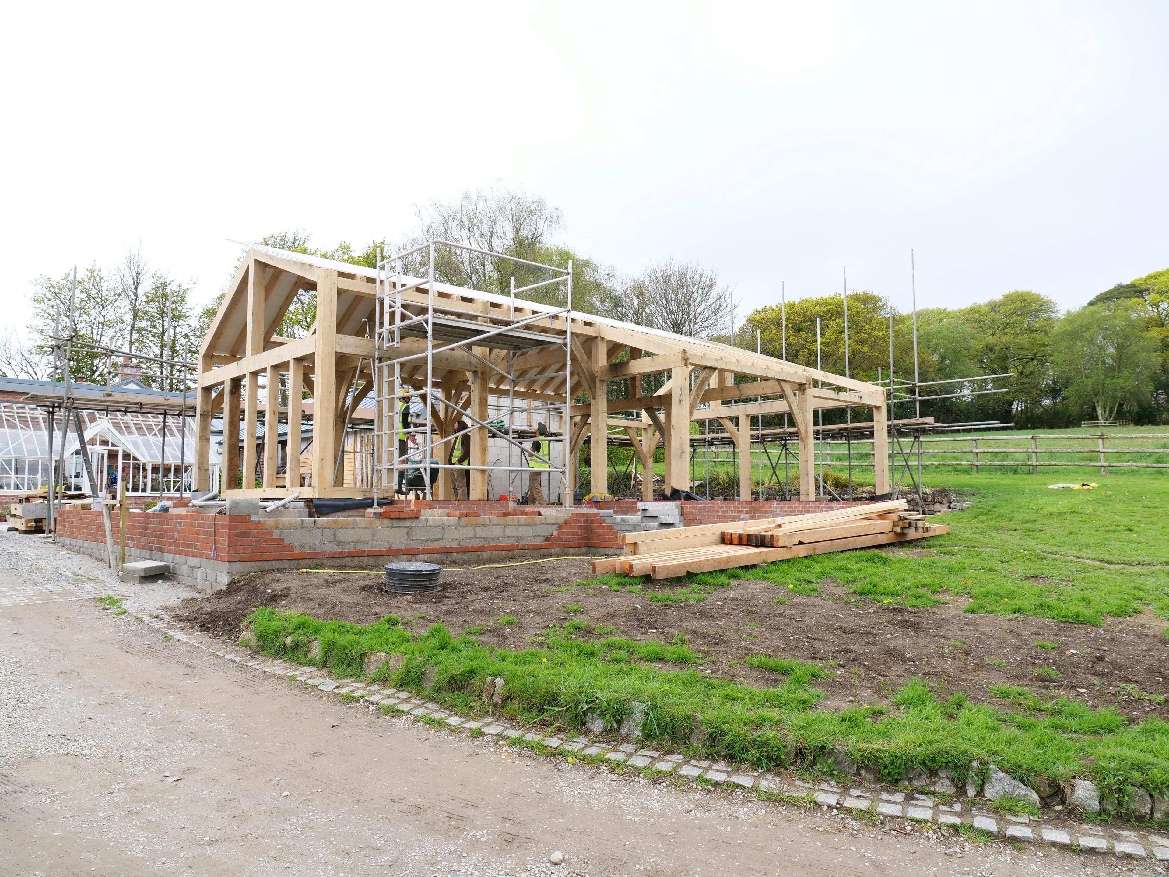 An oak frame being installed on a construction site with a green lawn around it