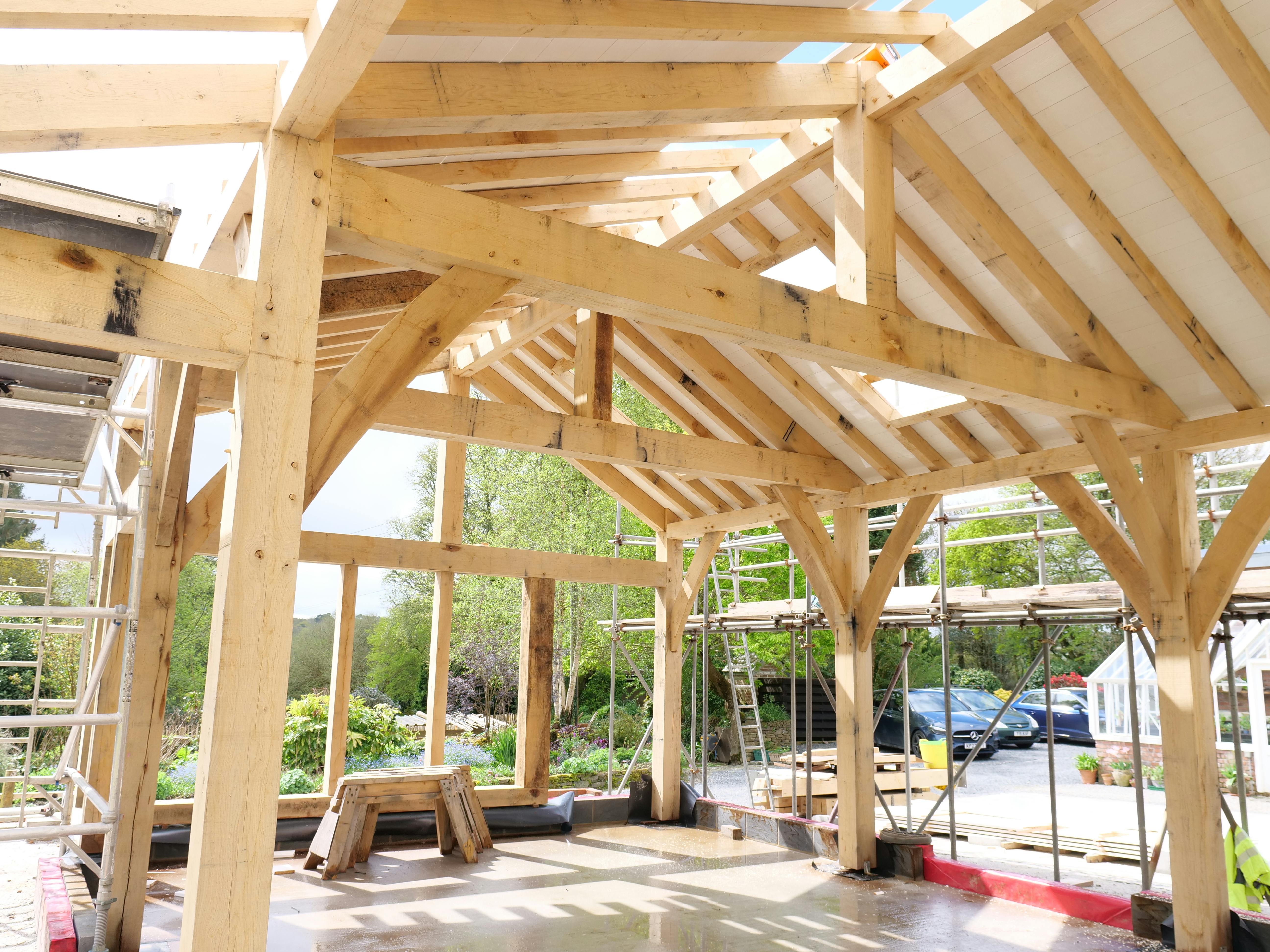 An oak frame being installed with white painted roof boarding