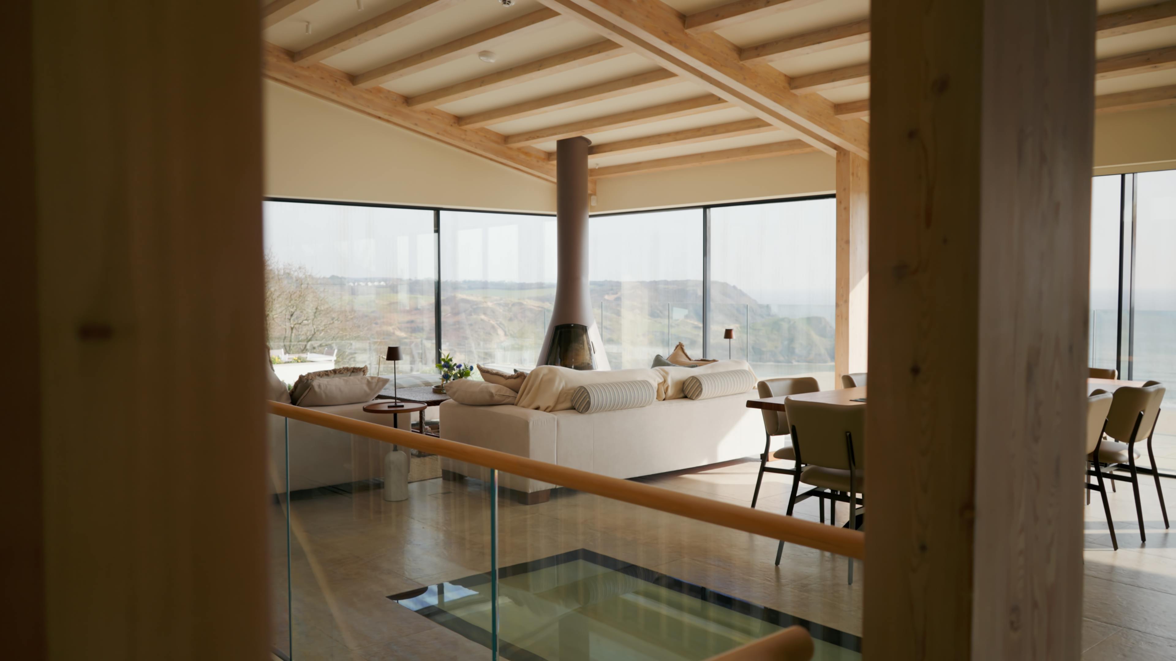 An oak glulam open plan living room with dining and lounge area, log burner and extensive glazing with views of the sea