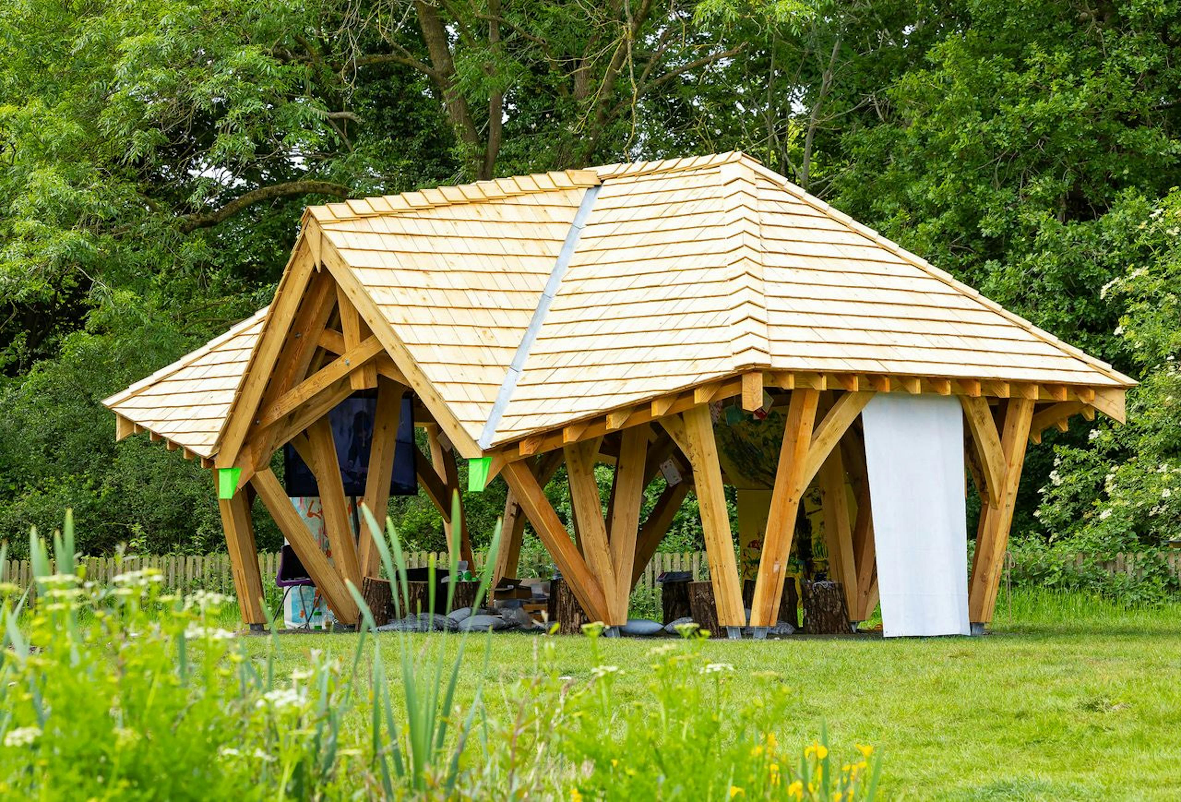 A timber structured outdoor classroom surrounded by a green lawn