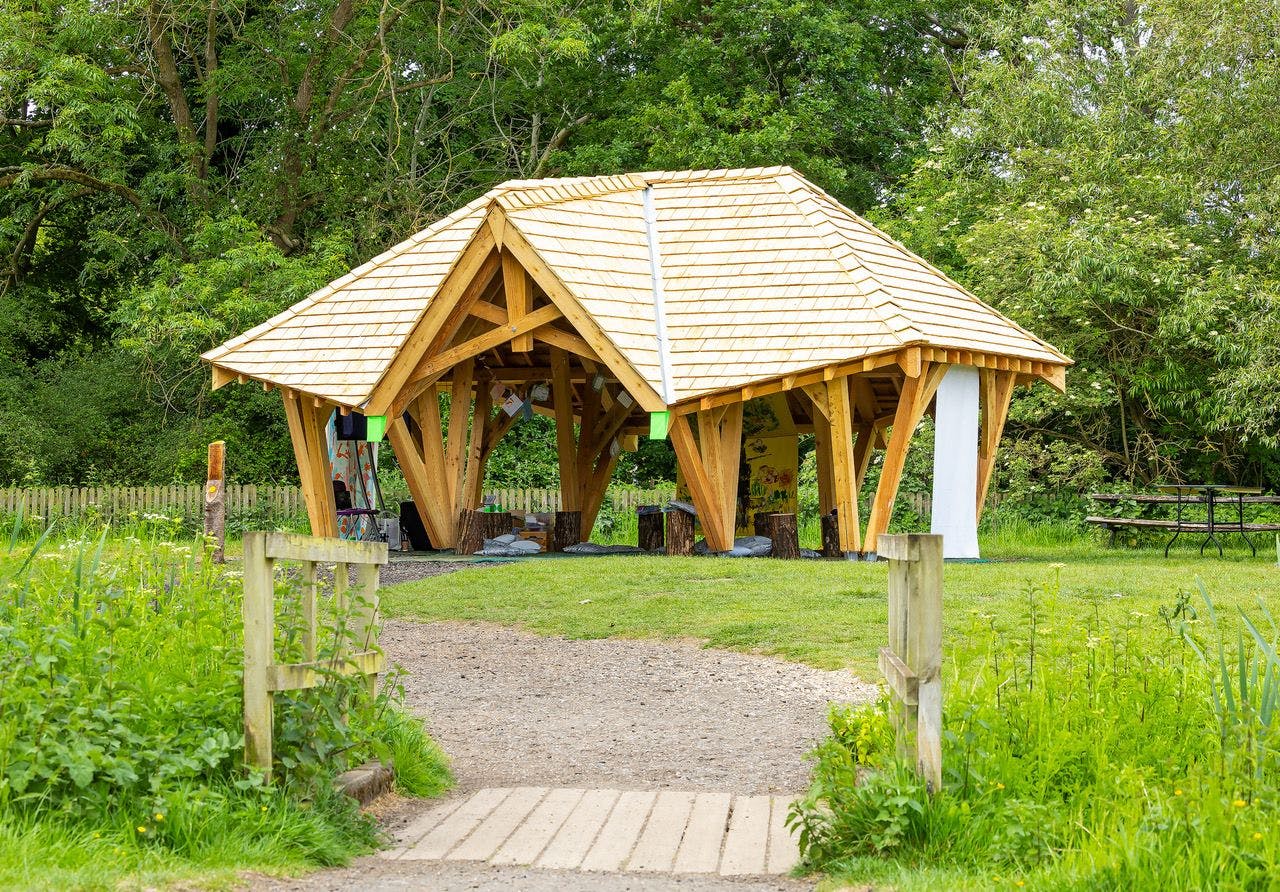 A timber structured outdoor classroom surrounded by a green lawn