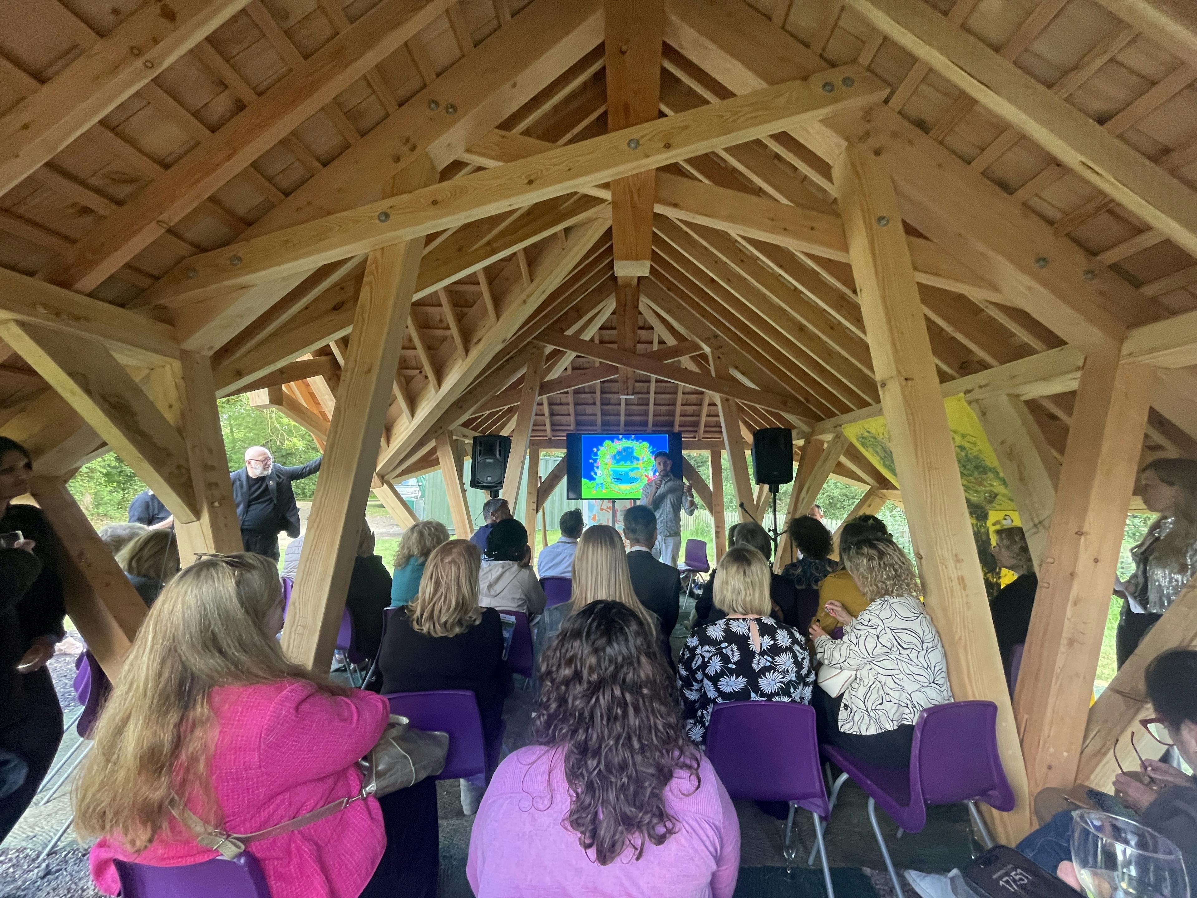 Adults sitting on chairs watching a presentation in a timber structured outdoor classroom