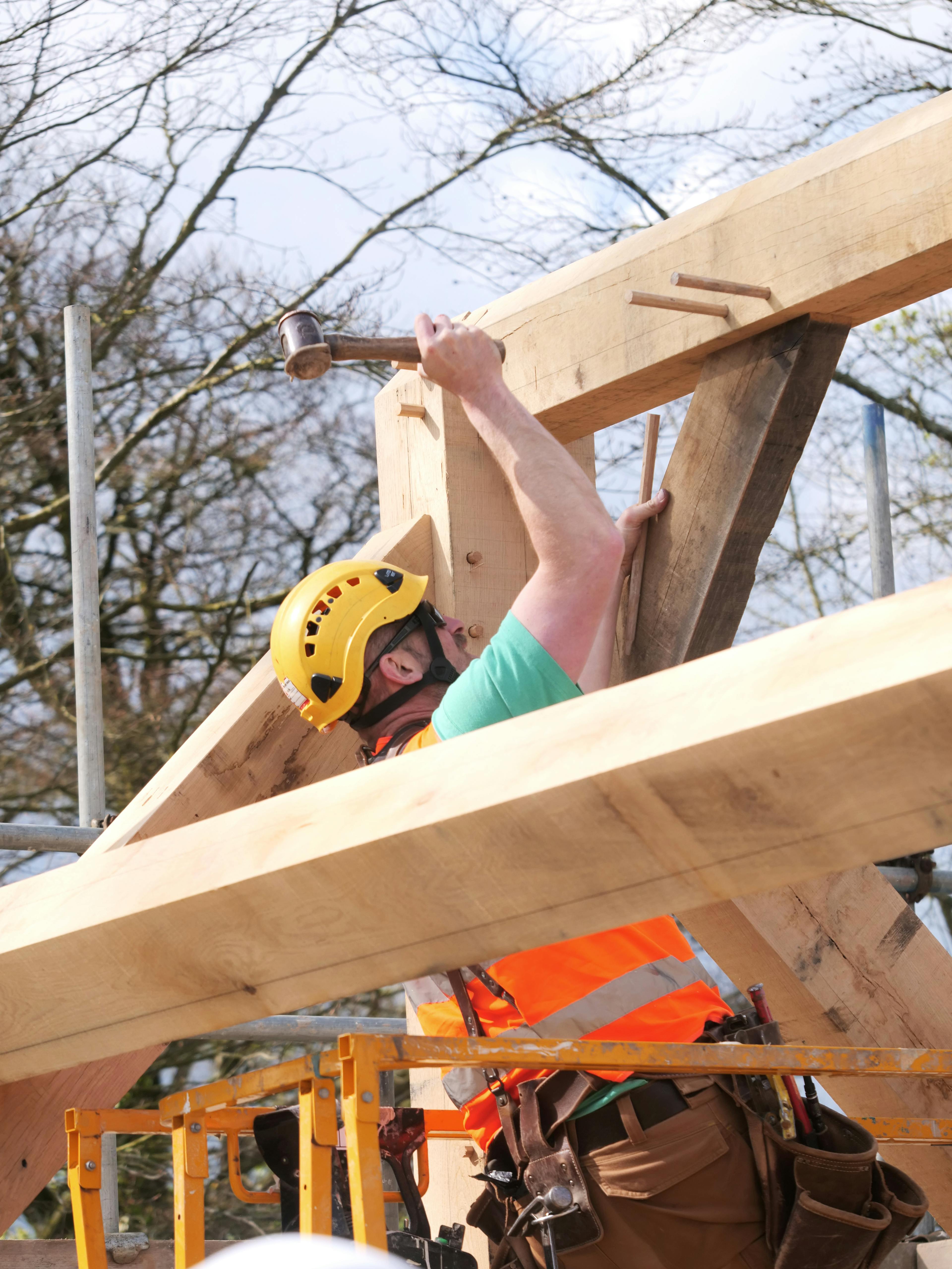 A carpenter knocks in wooden pegs on an oak frame for a wedding barn