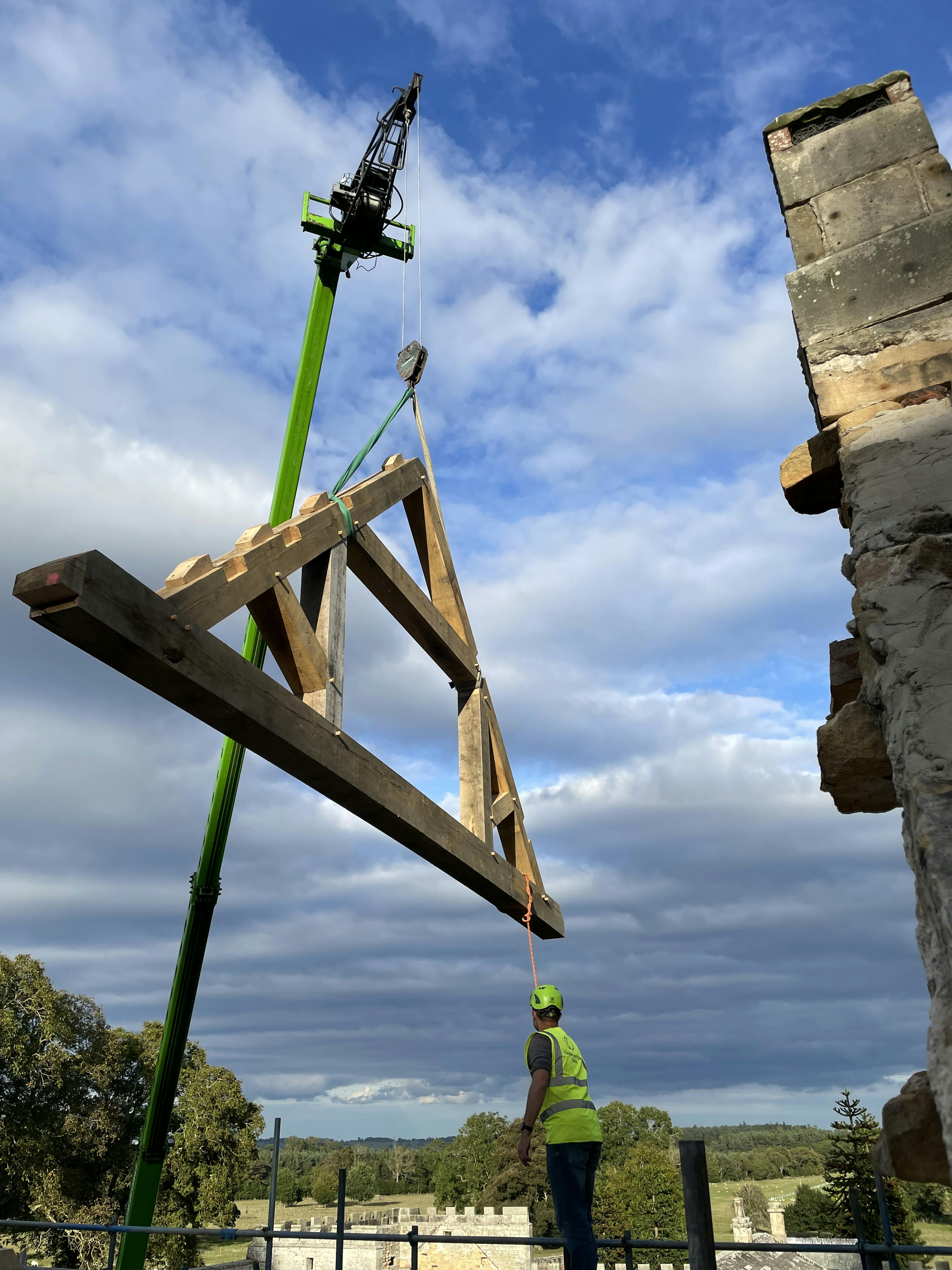 A crane lifts into place an oak frame truss for a renovated coach house to create a new cafe for visitors to Belsay Hall