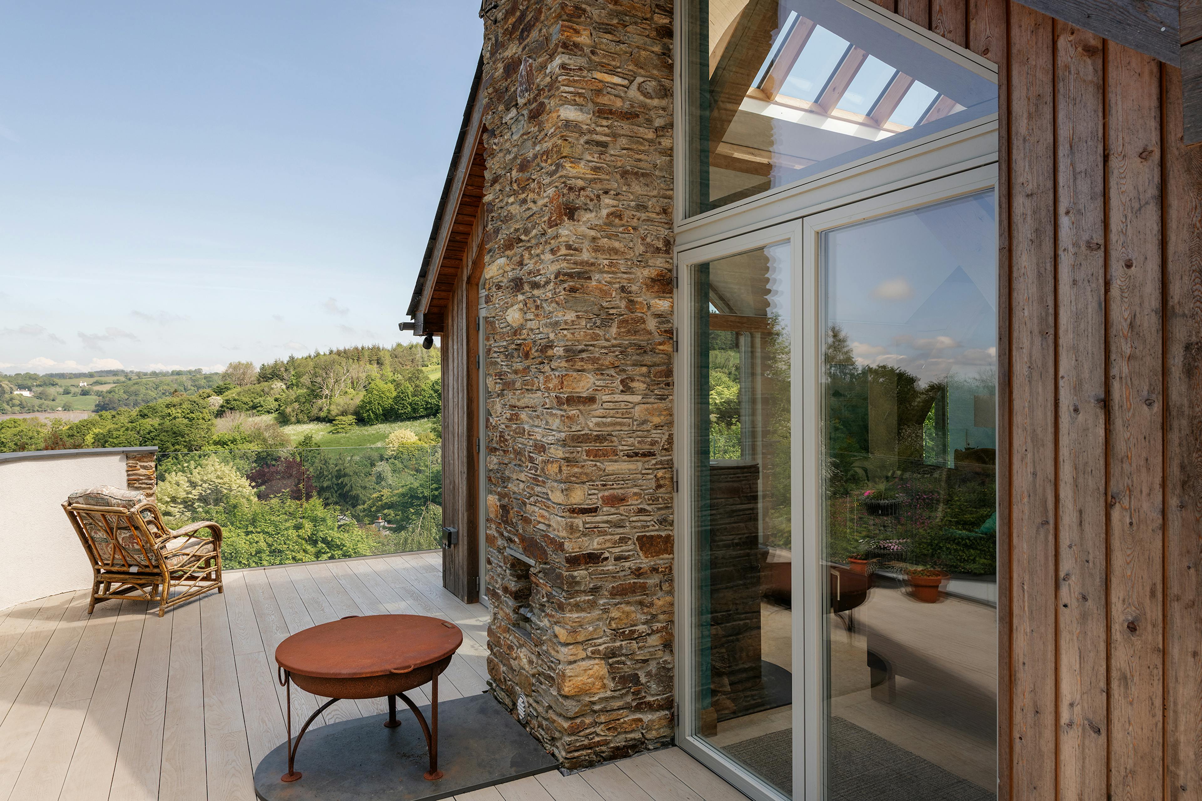 The terrace of an oak framed reverse level home with stone cladding and views of an estuary
