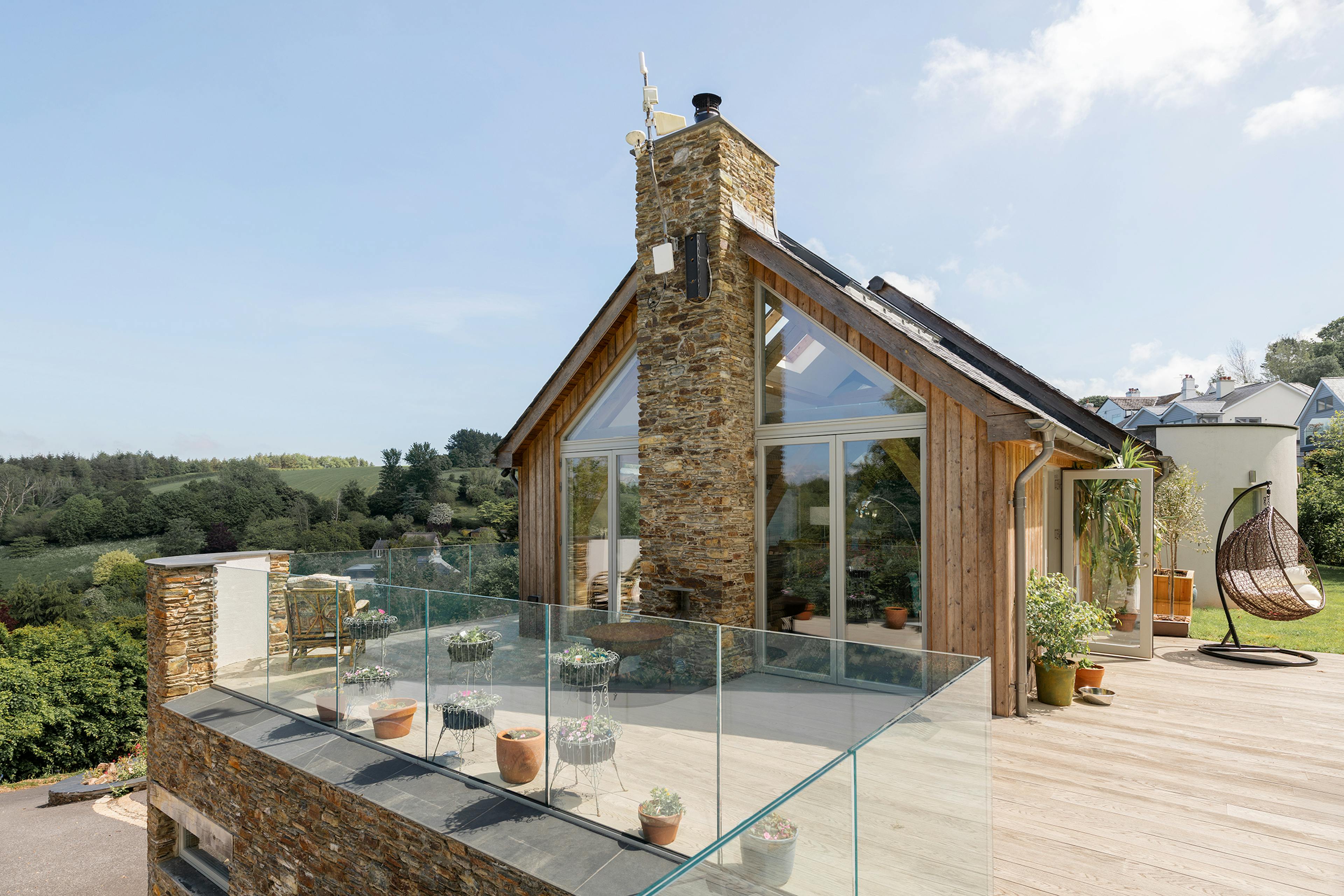 The terrace of an oak framed reverse level home with stone cladding and views of an estuary