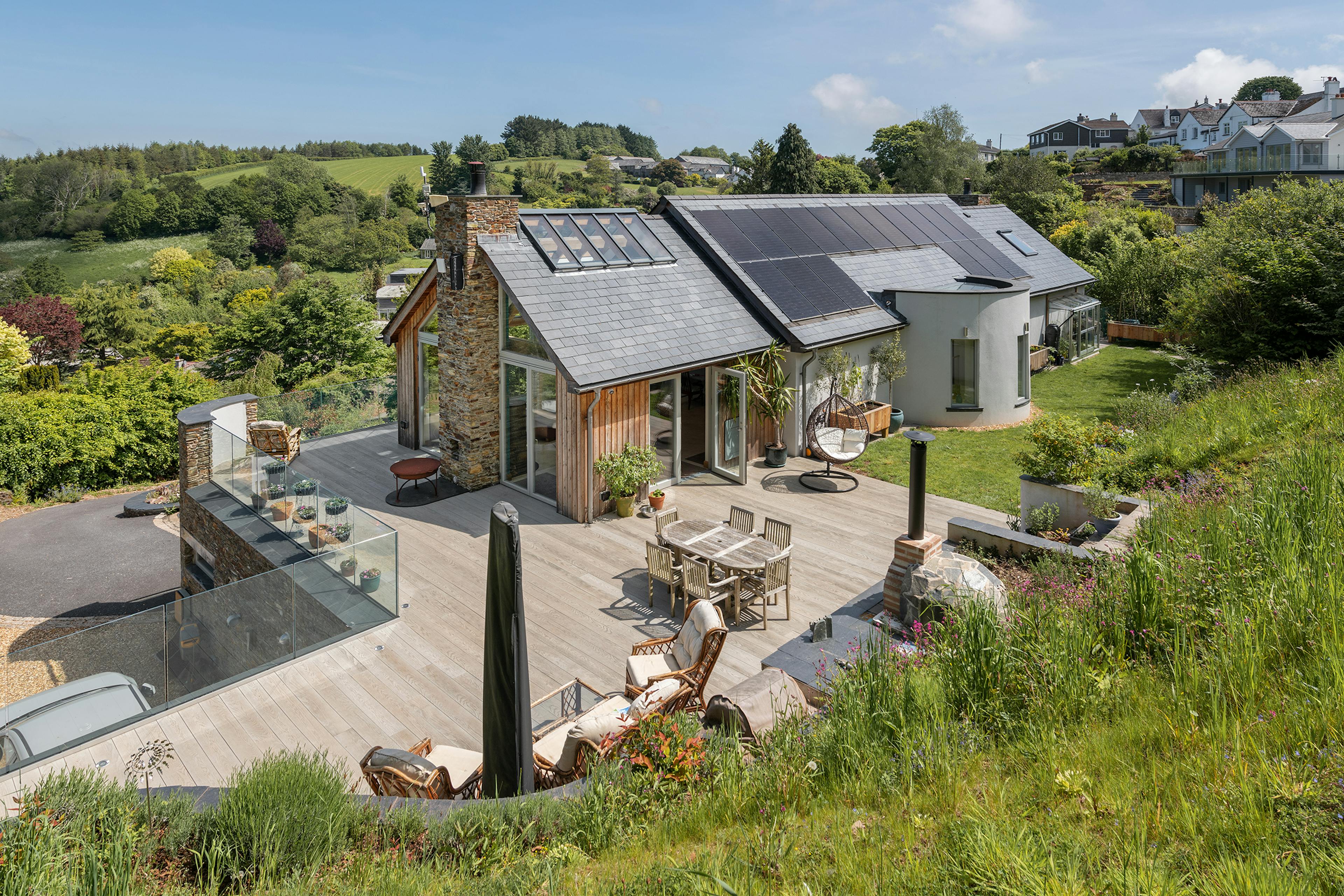 The terrace and back garden of an oak framed reverse level home with stone cladding and views of an estuary