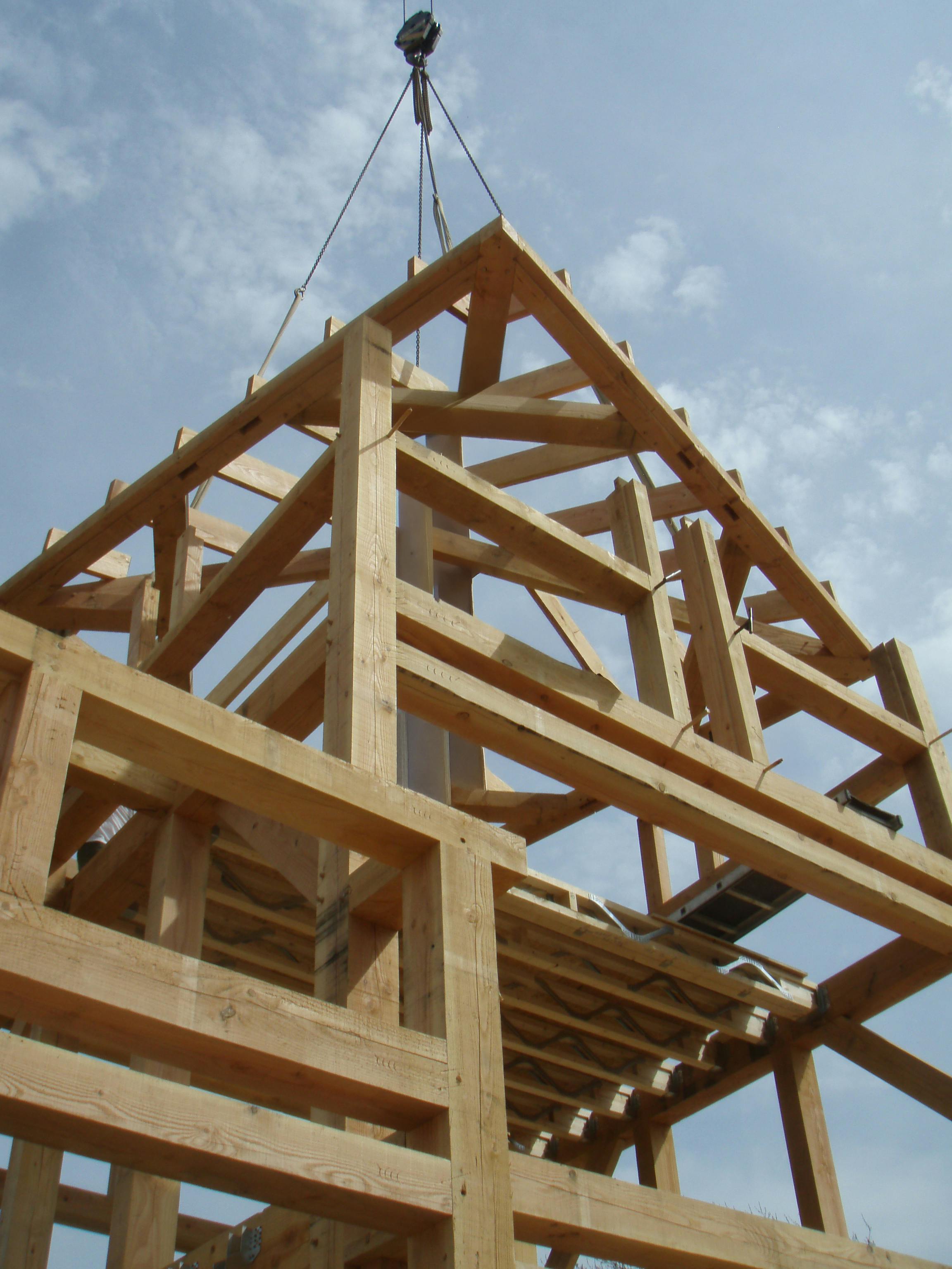 Construction crew erecting a Douglas fir timber frame, carefully lowering a preassembled roof section into place with a crane.