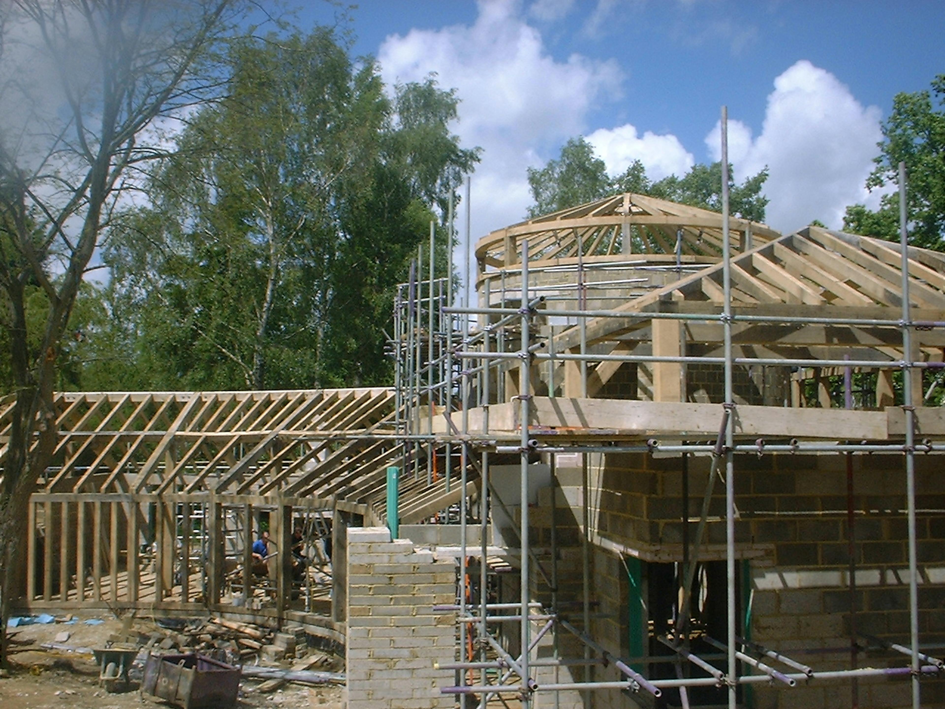 Construction site showing the assembly of a large oak timber frame structure, with visible beams and framework in progress