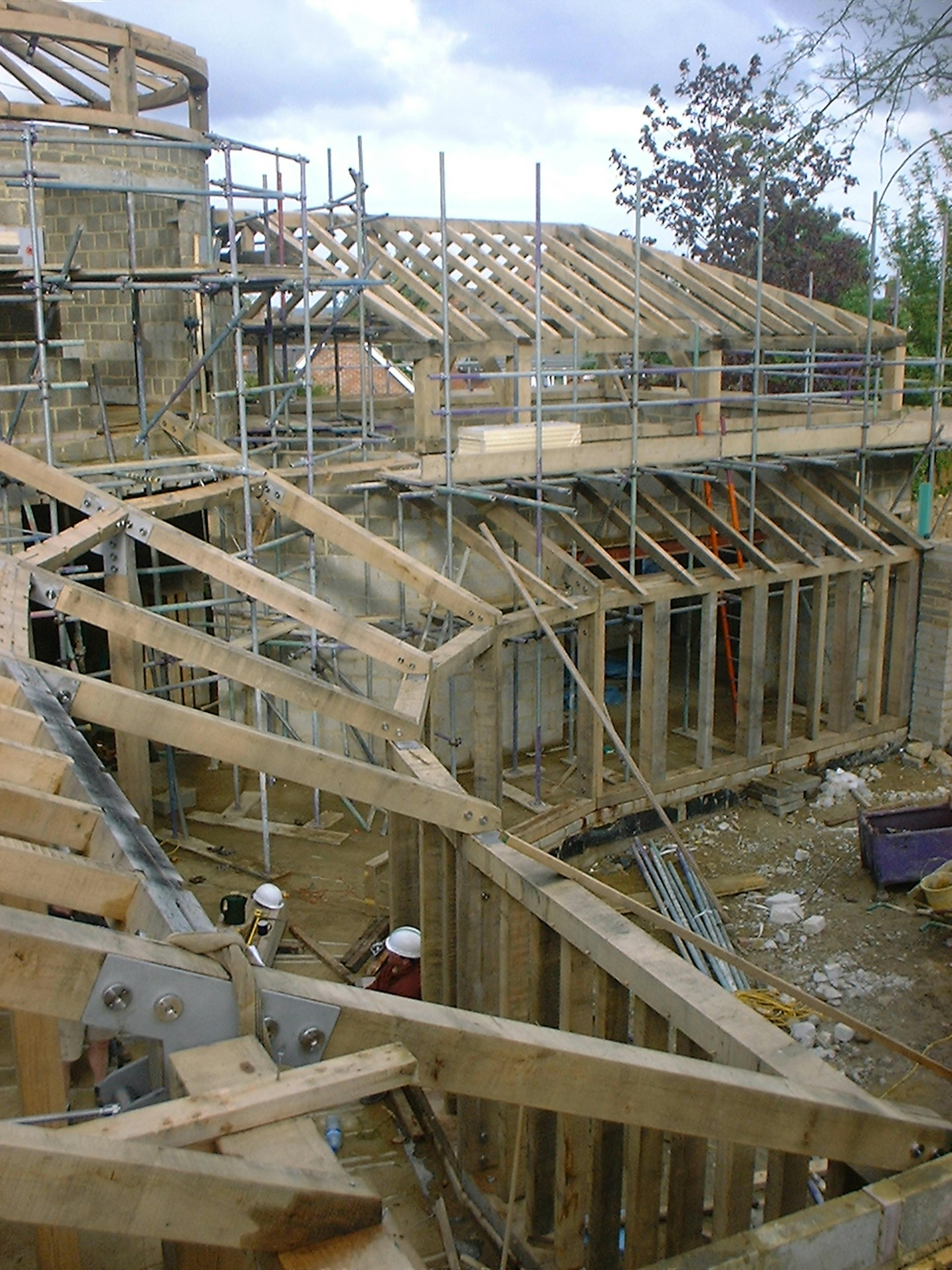 Construction site featuring a curved oak timber frame structure in progress, showcasing the bending craftsmanship of the wooden beams