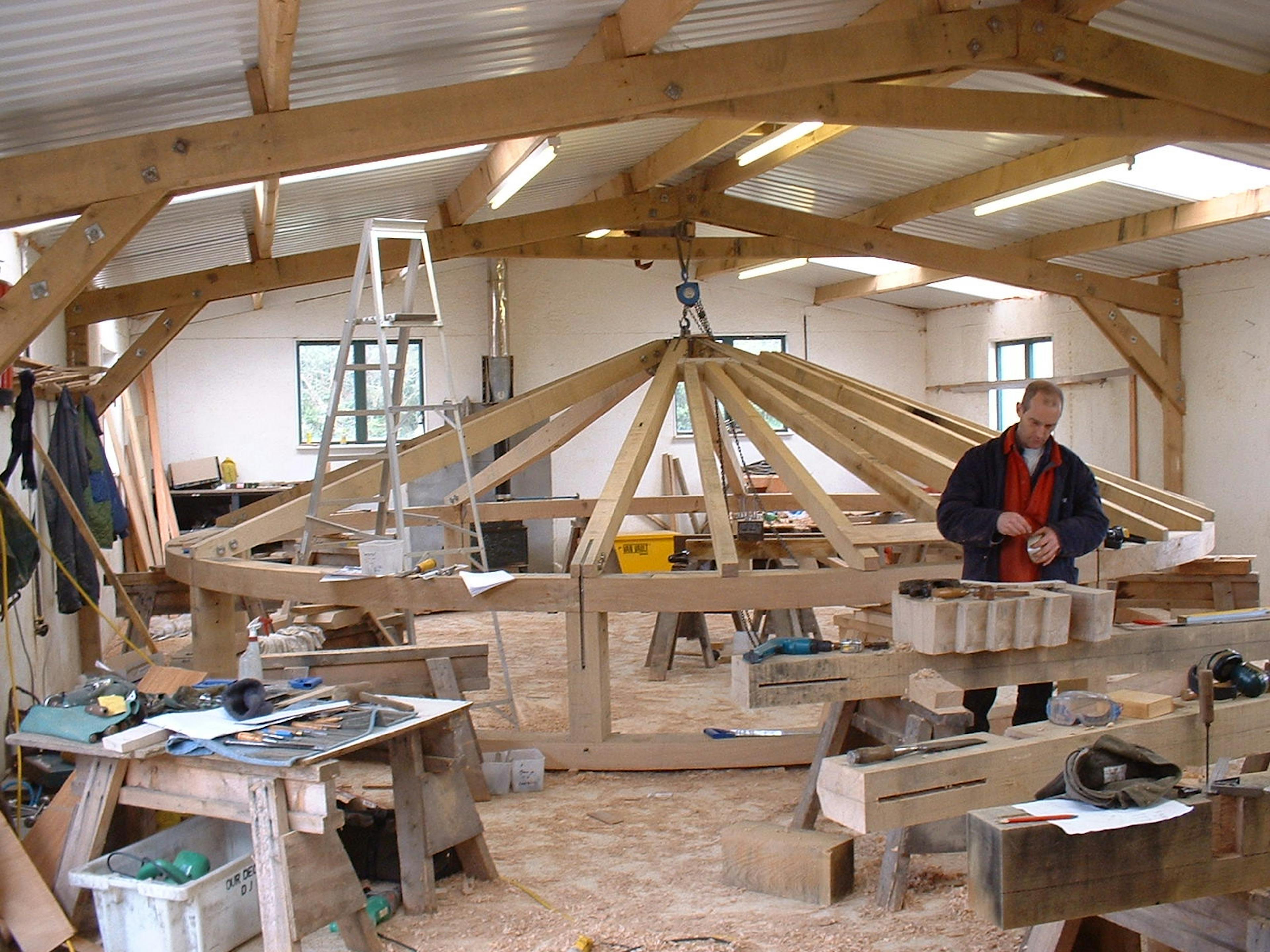 Workshop scene showing the assembly of a timber roof structure, with workers fitting beams and joints together during construction
