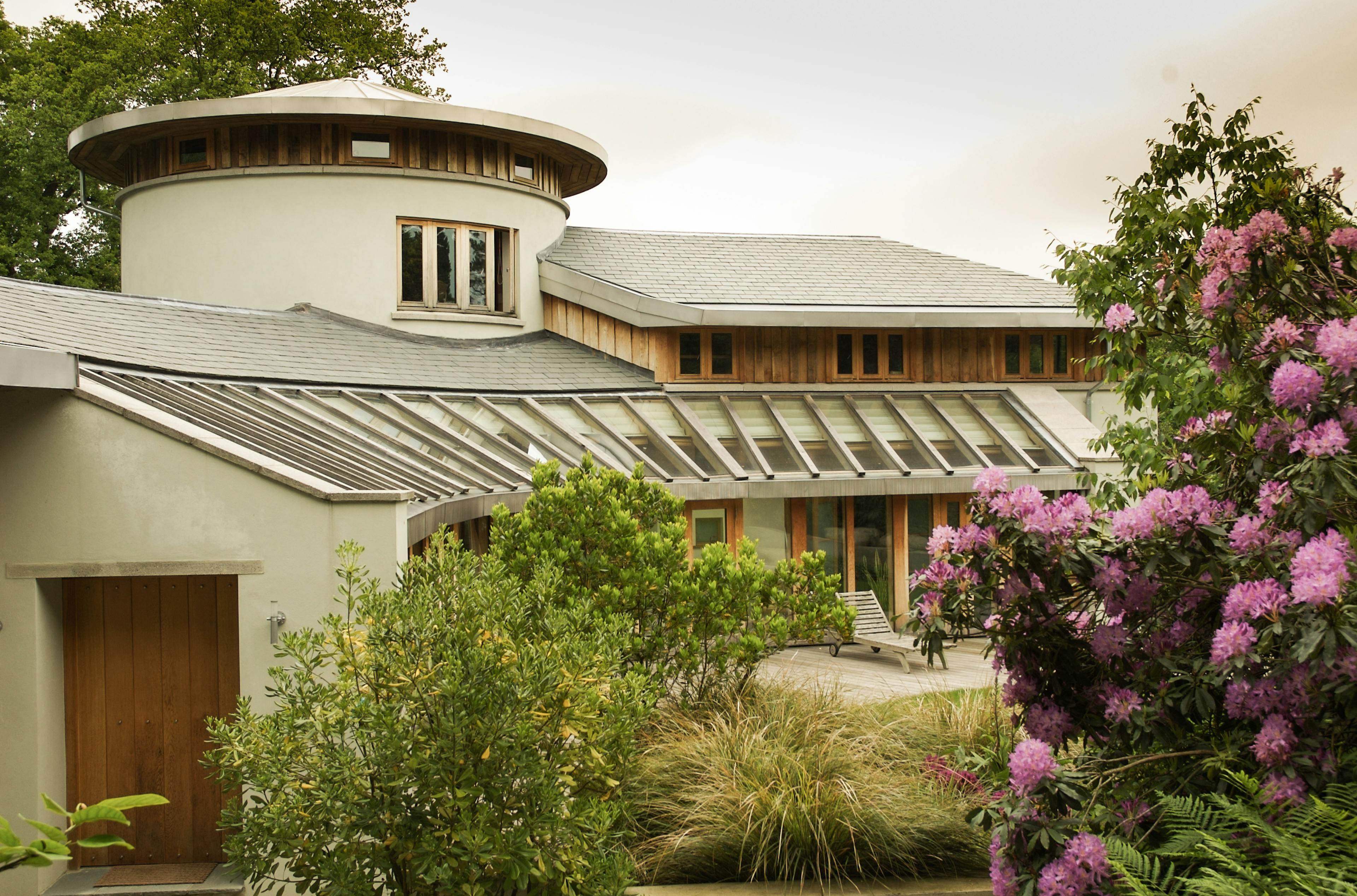 Exterior view of an oak-framed house with floor-to-ceiling glazing and a gently curved façade, blending traditional timber craftsmanship with contemporary design