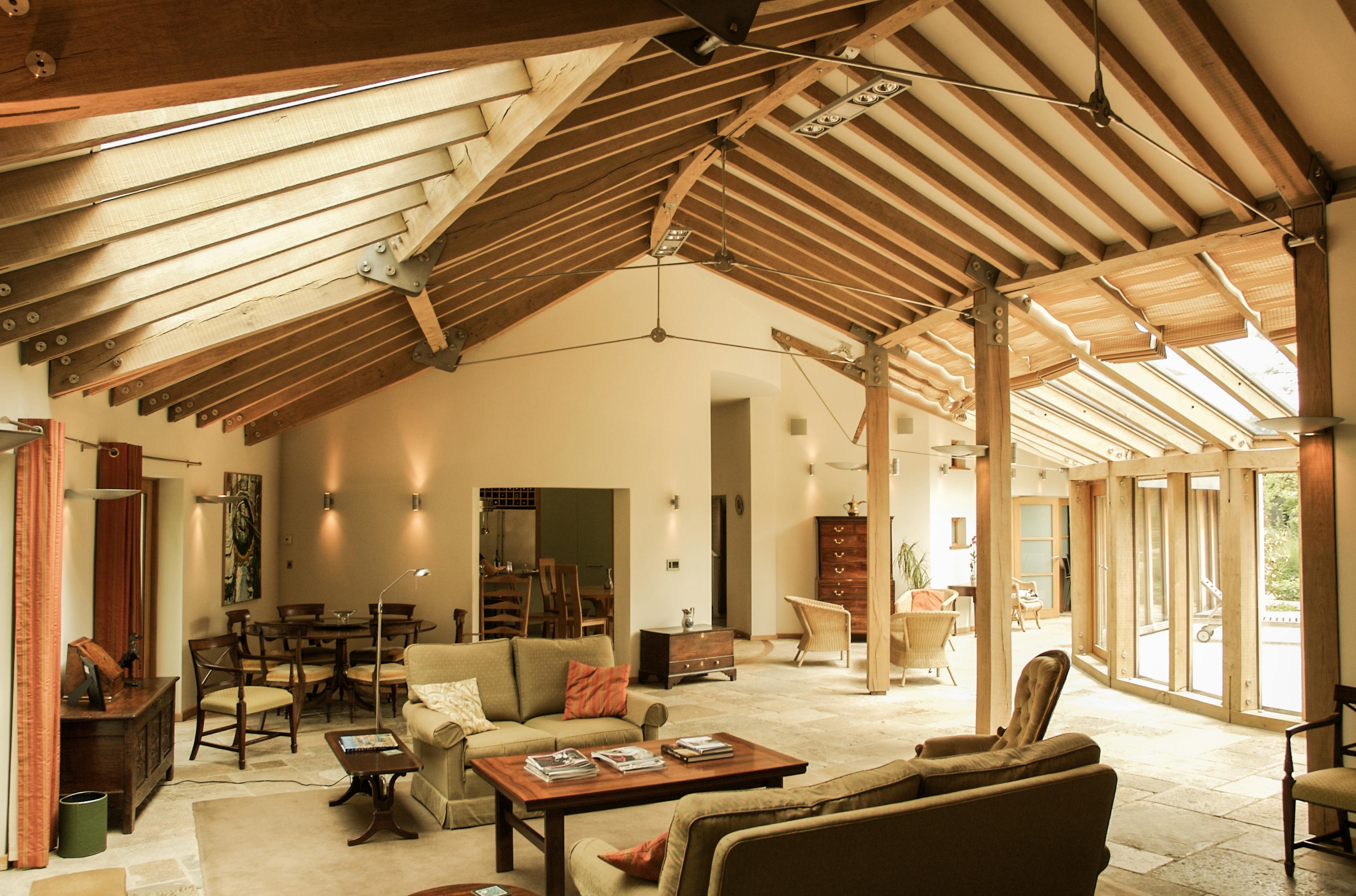 Finished oak-framed house living space with exposed timber beams, cozy seating area, and large windows allowing natural light to fill the room