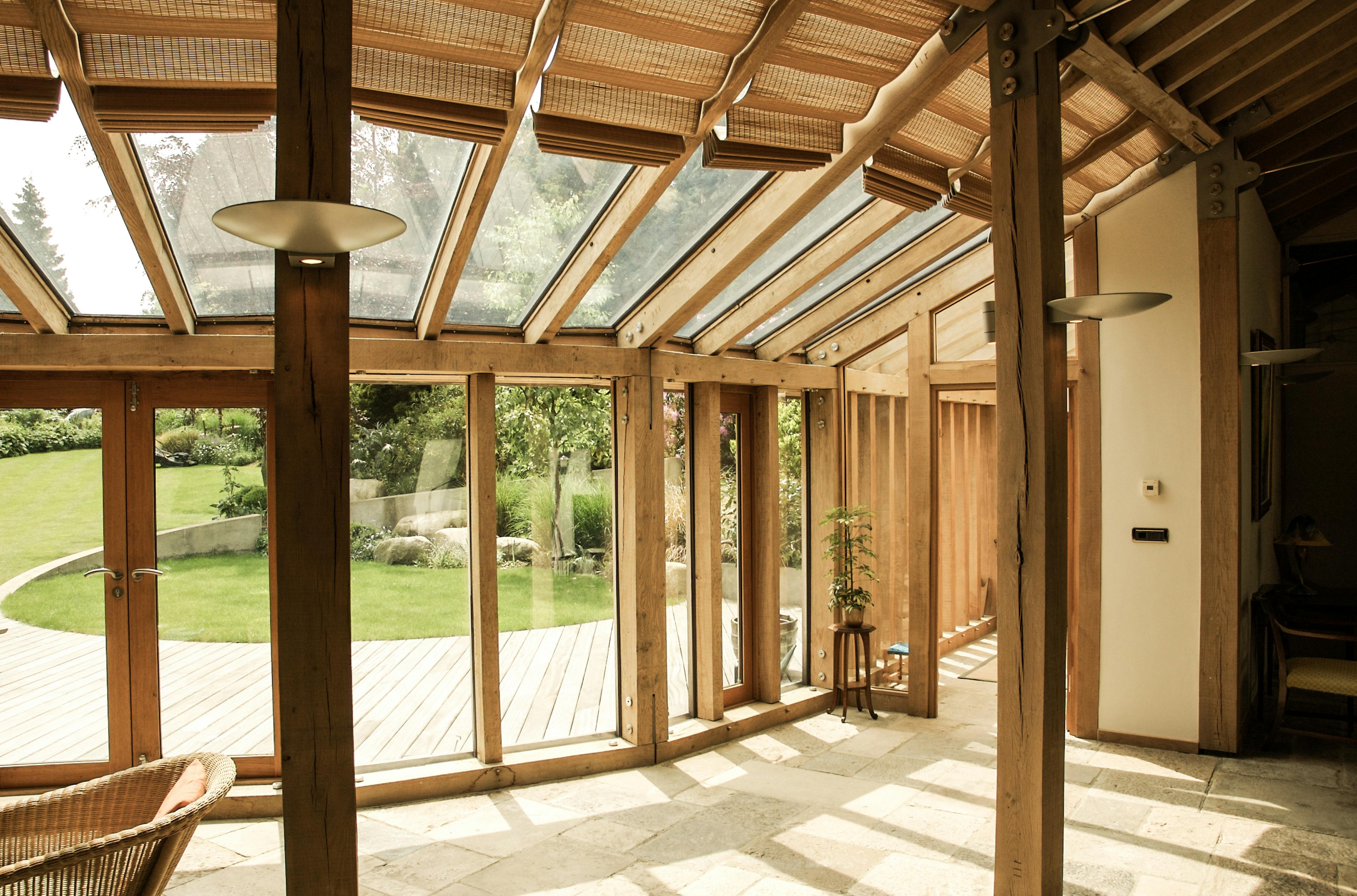 Interior view of a walkway in an oak-framed house with large glass panels allowing natural light to fill the space, framed by exposed timber beams