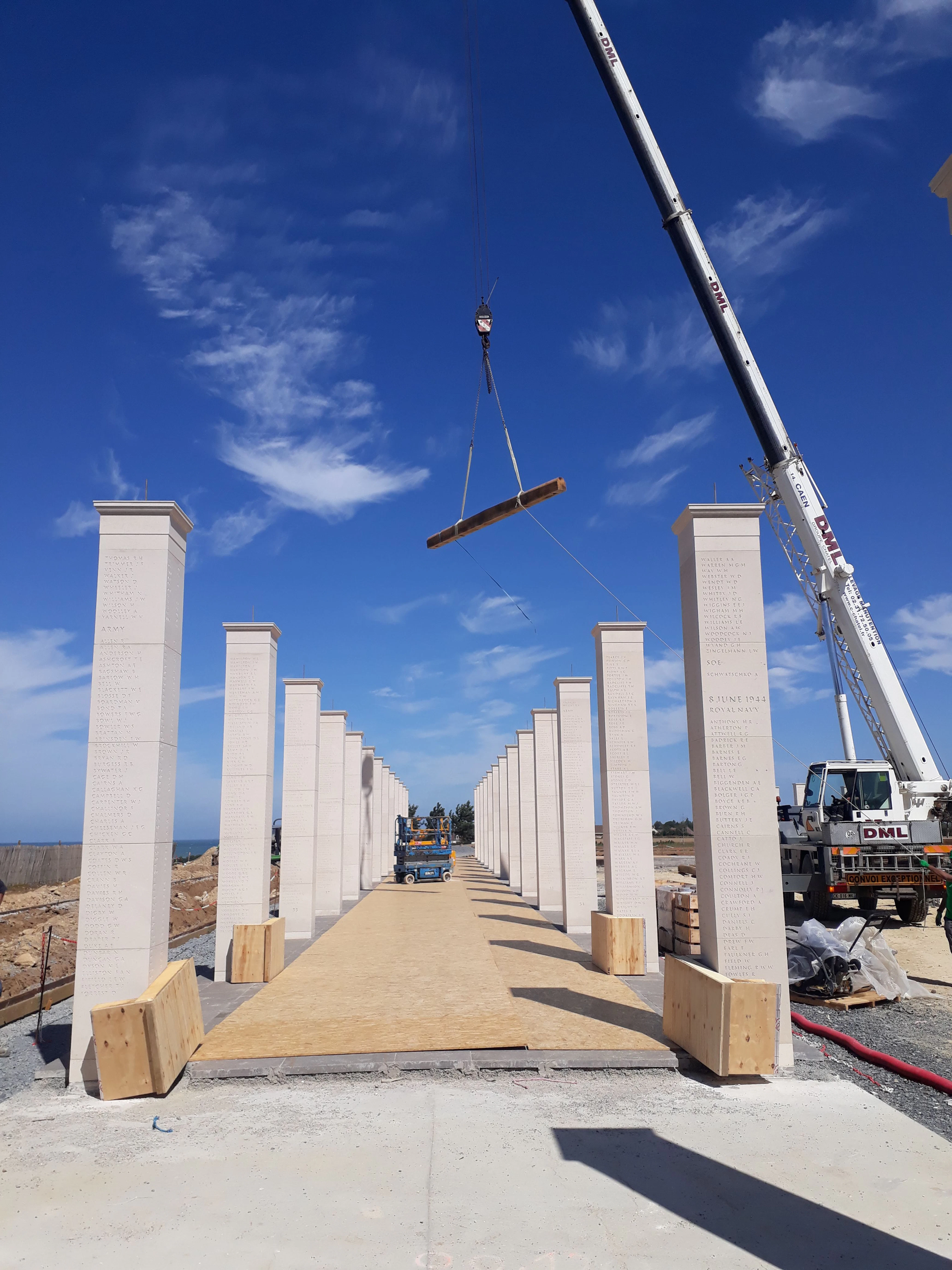 Crane lifting structural timber components on site during the British Normandy Memorial pergola construction, with Oak Larch team members coordinating the operation