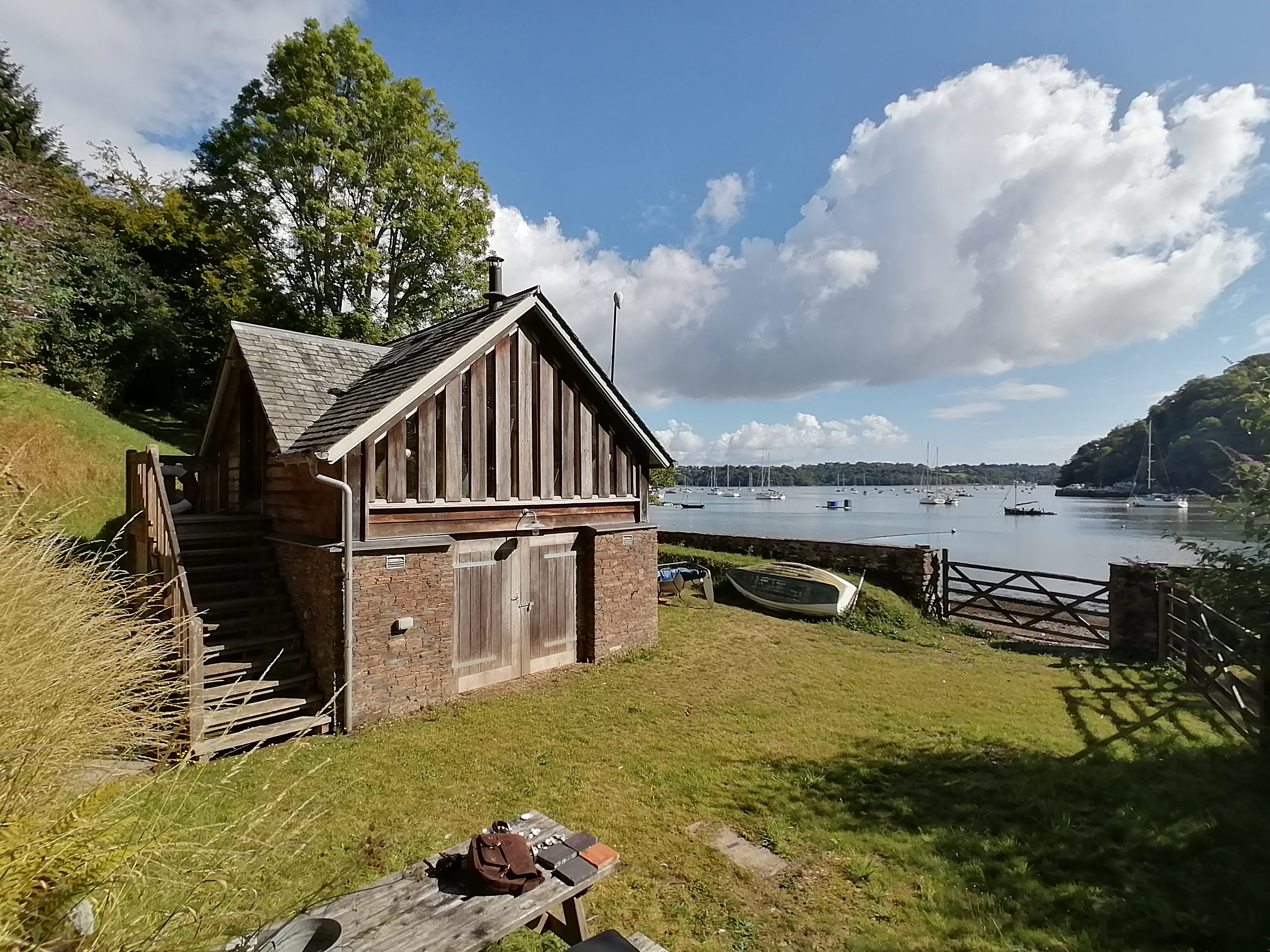 Rear exterior view of a coastal cottage with oak frame detailing, showing the back entrance set against a natural shoreline backdrop