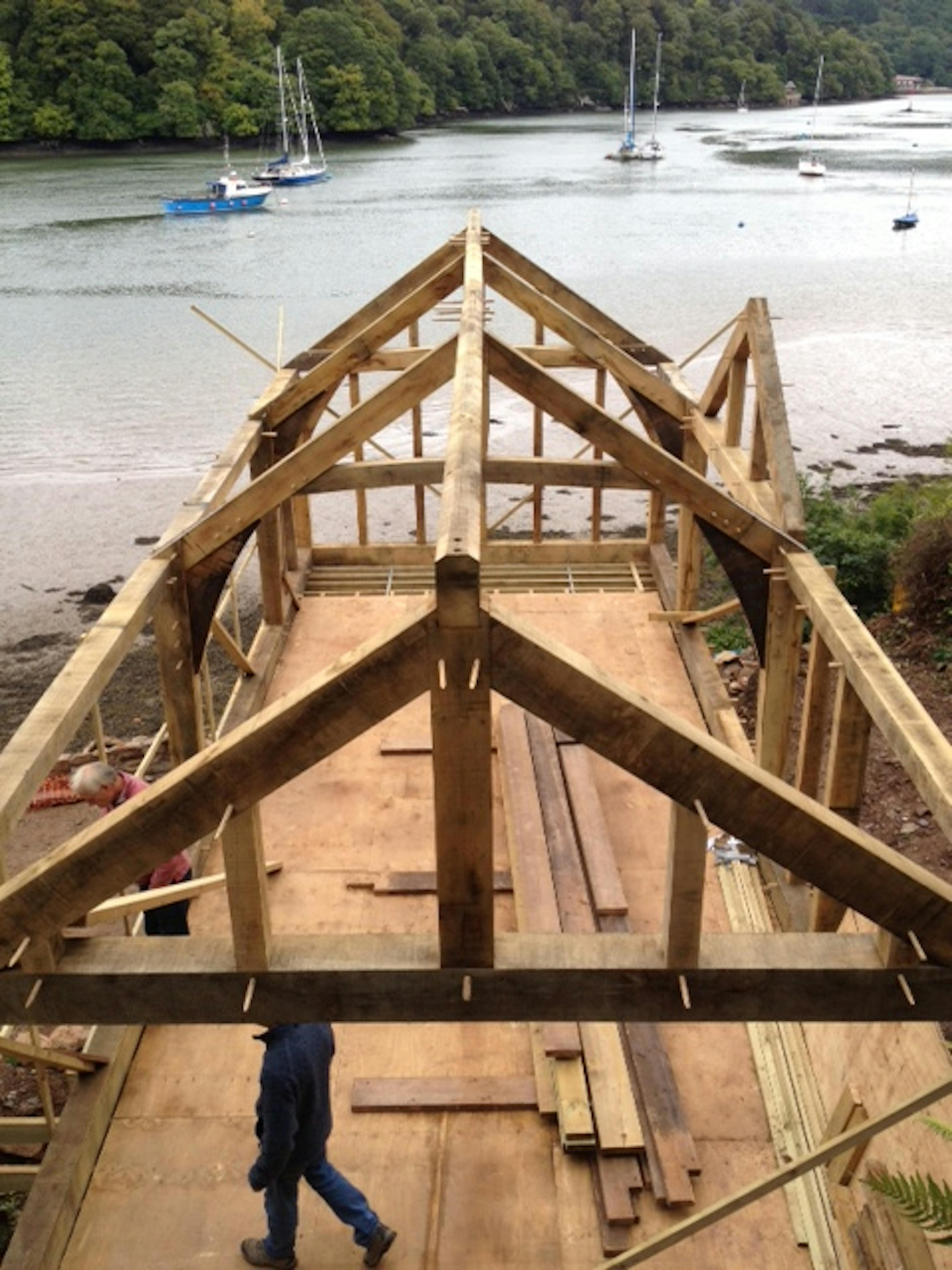 Partially completed oak frame structure at a coastal cottage site, with visible timber beams and open framework
