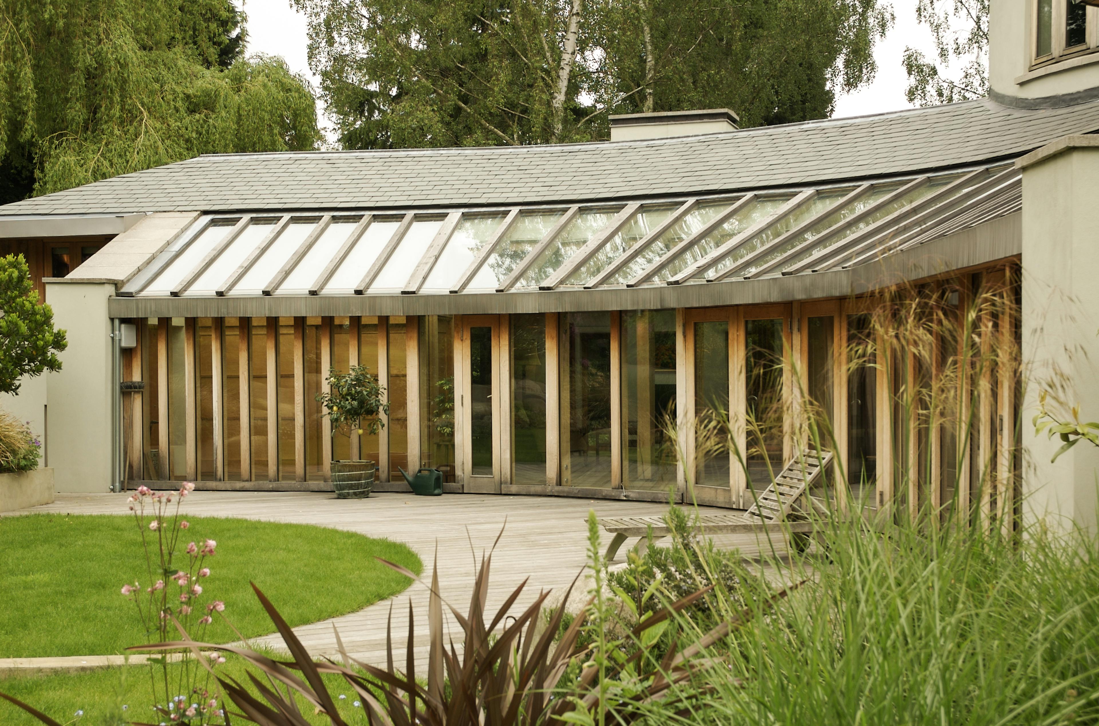 Exterior view of an oak timber frame house featuring expansive curved glazing along a gently winding walkway, blending natural materials with contemporary design