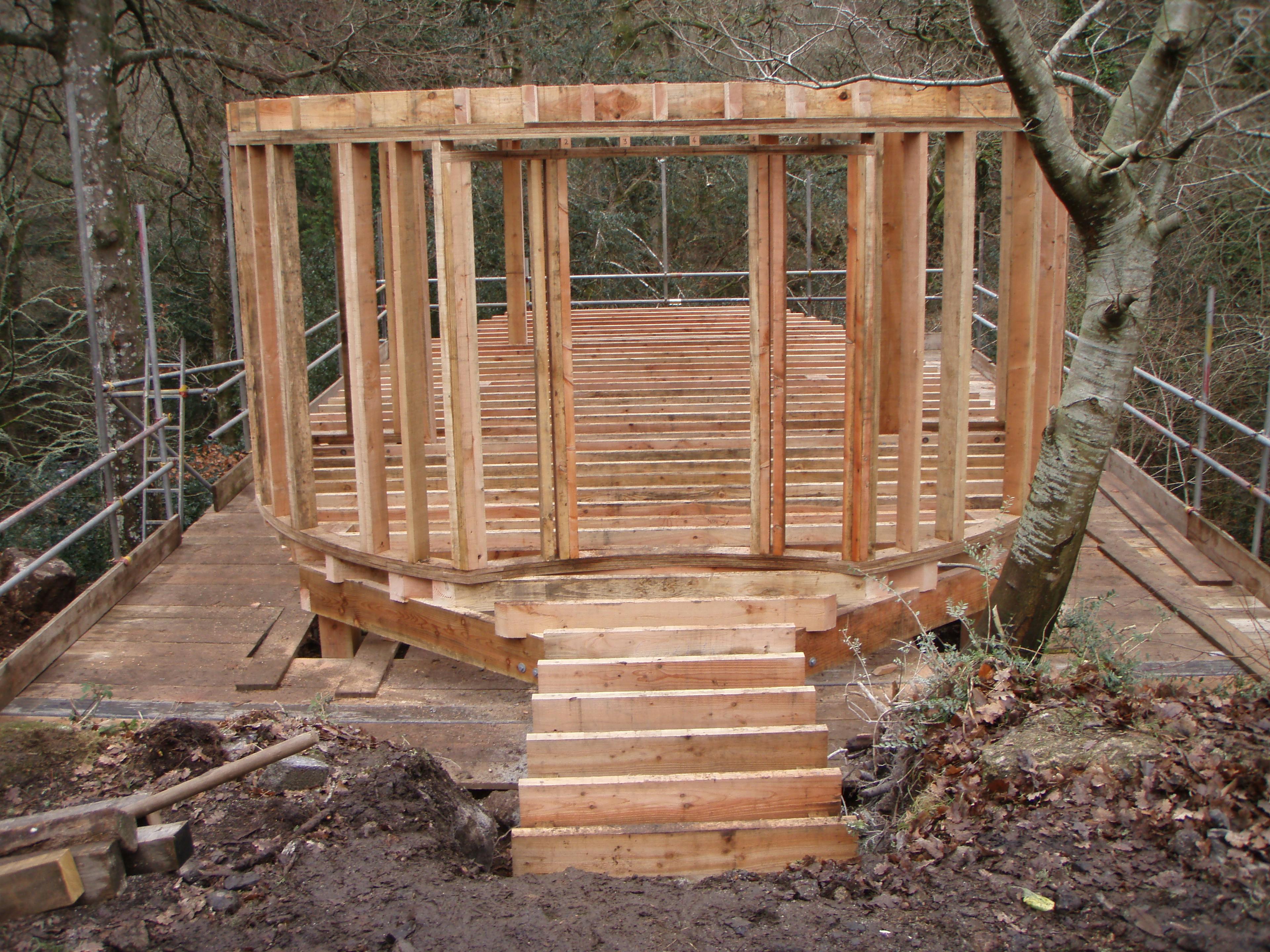 Construction site of a treehouse in Dartmoor, showing the assembly of a Douglas fir timber frame structure with exposed beams