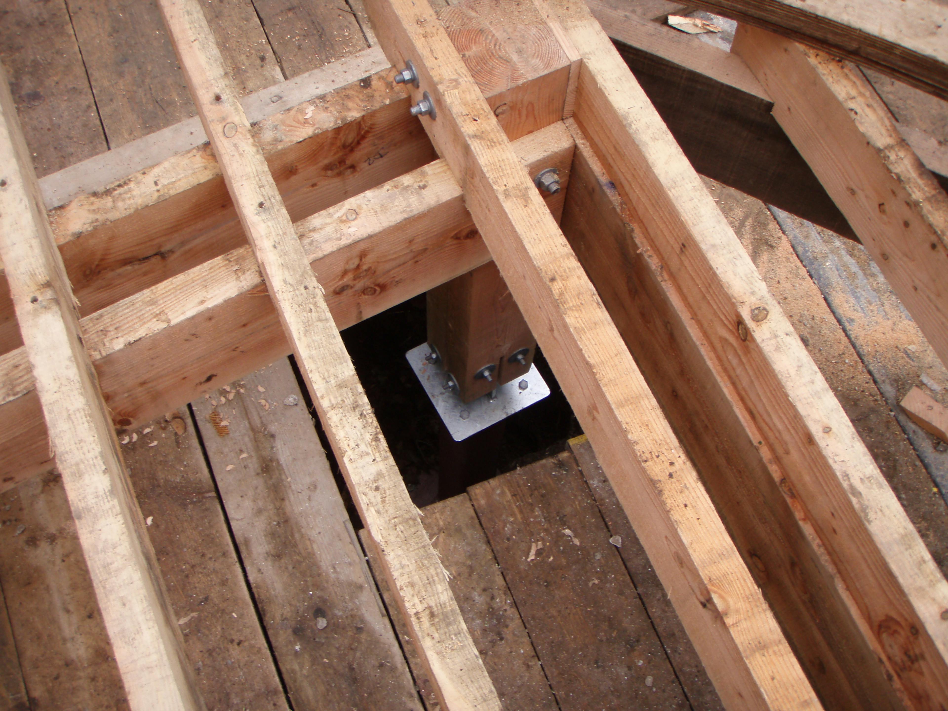 Close-up of steel post feet anchoring Douglas fir timber posts during the assembly of a treehouse structure at a Dartmoor site