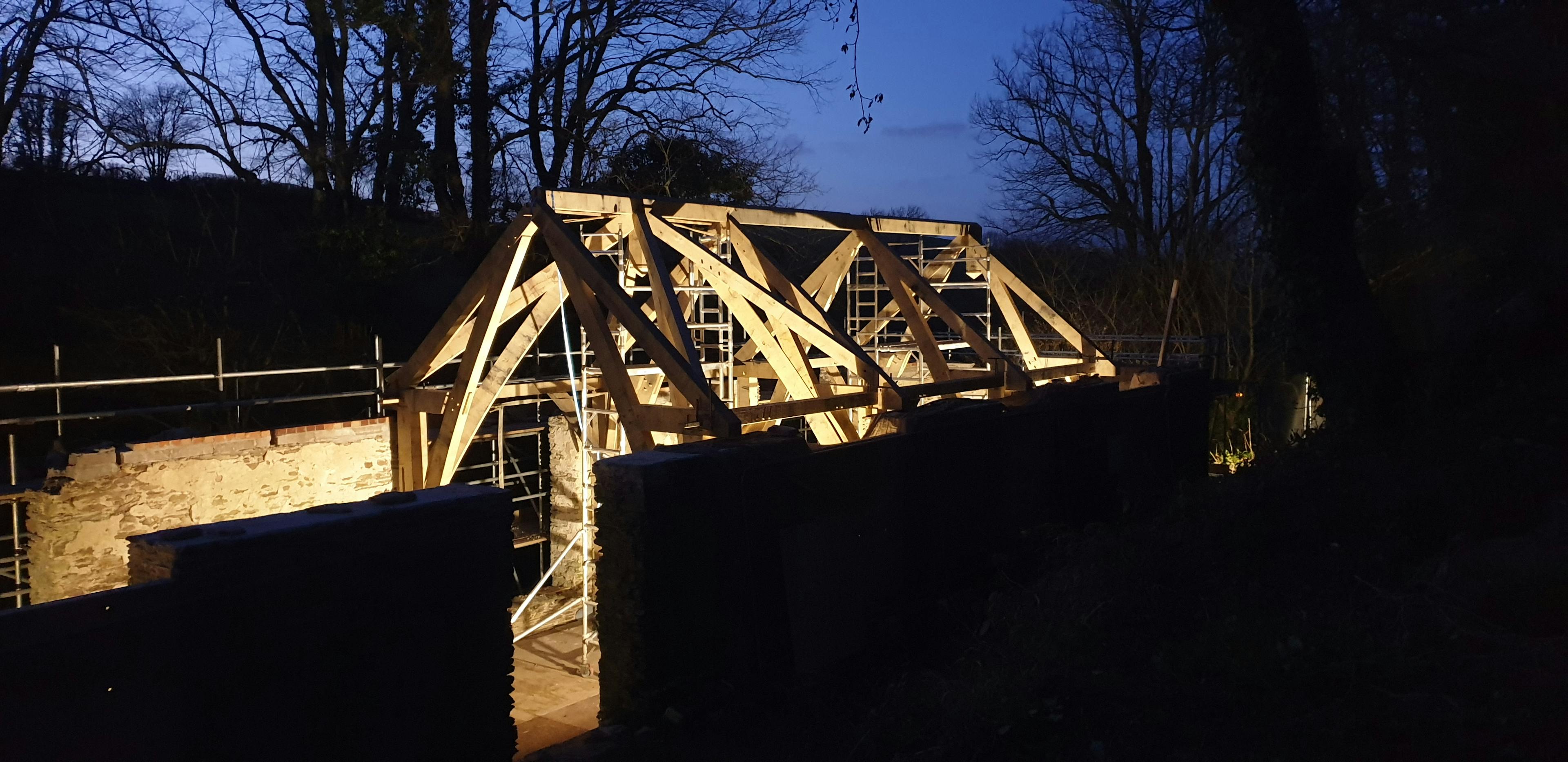 Timber frame structure under construction at dusk, surrounded by scaffolding