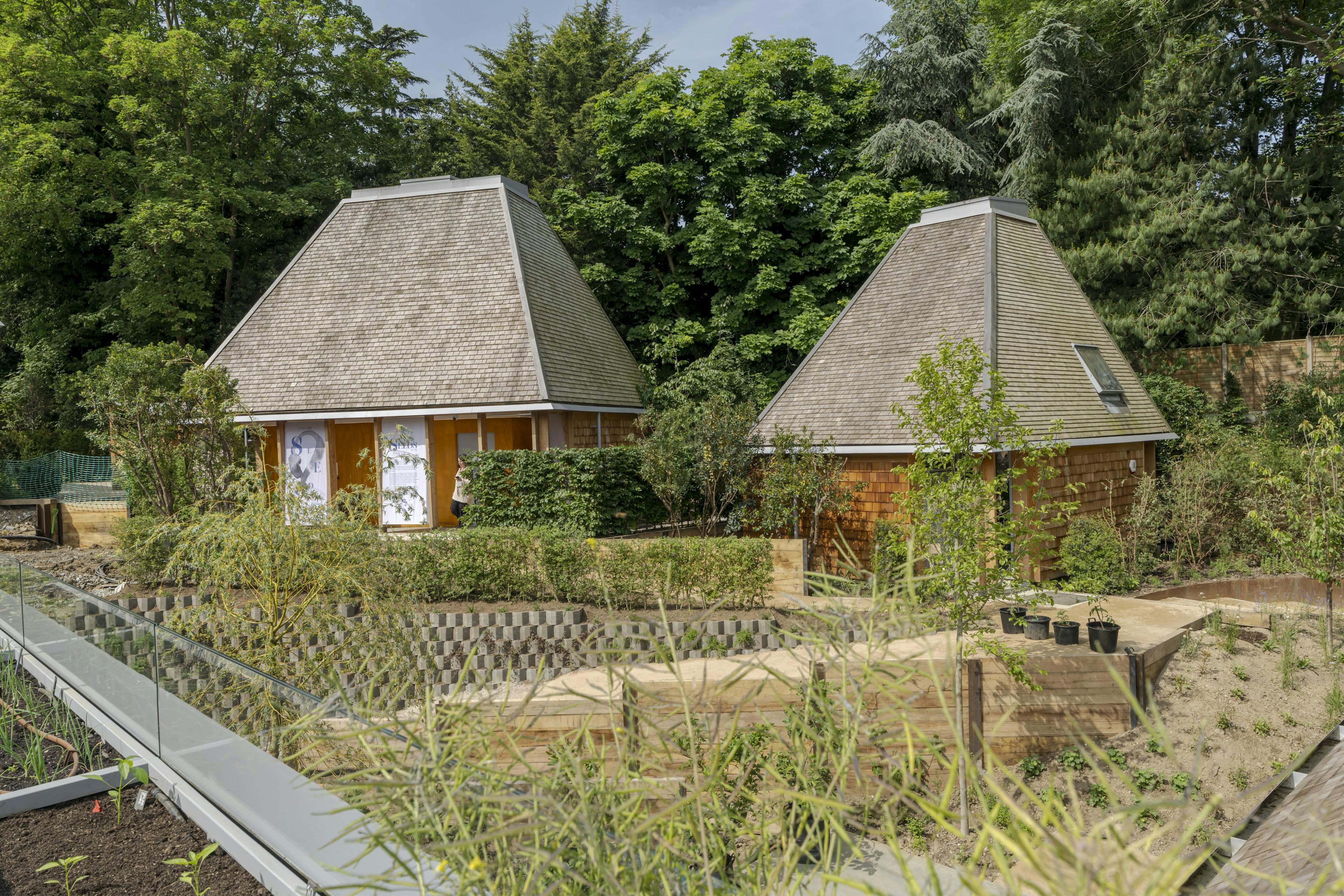 Exterior view of multiple event structures with exposed Douglas fir frames, arranged within a landscaped garden, highlighting natural materials and open design