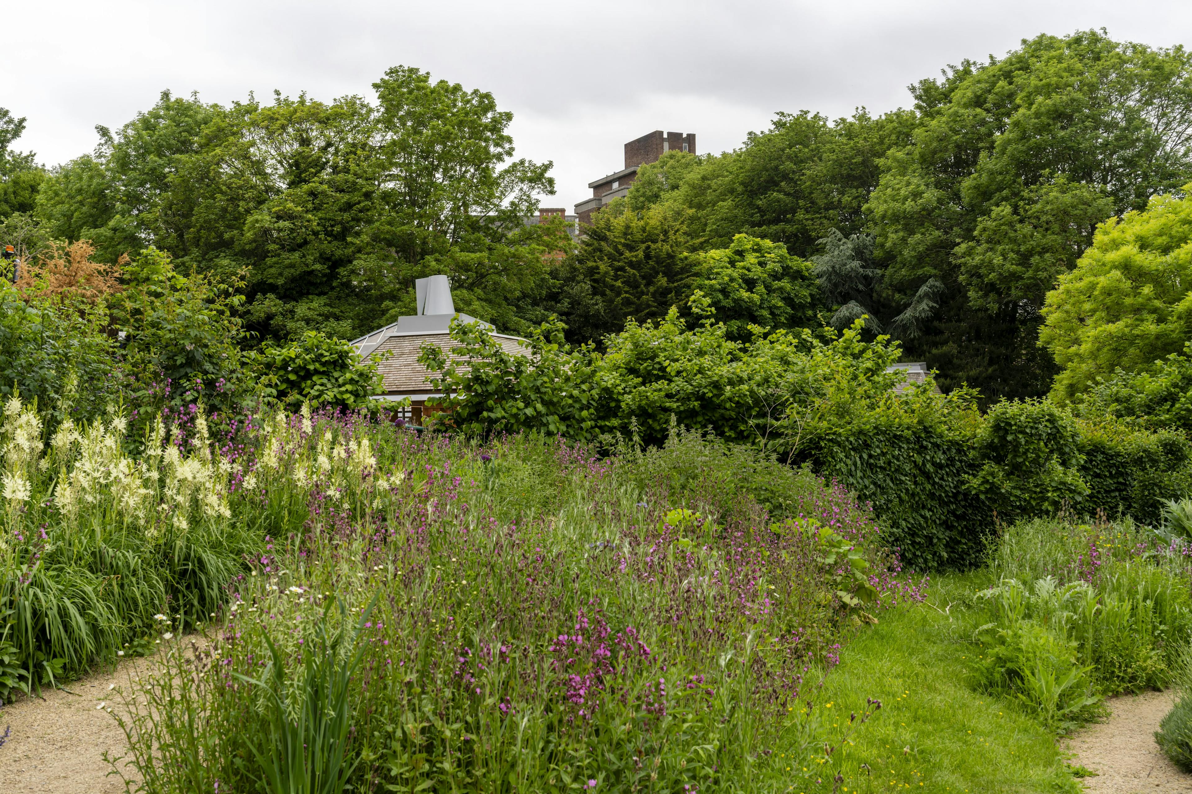 Exterior view of an event venue surrounded by lush gardens, featuring timber-framed structures integrated into the landscaped outdoor setting