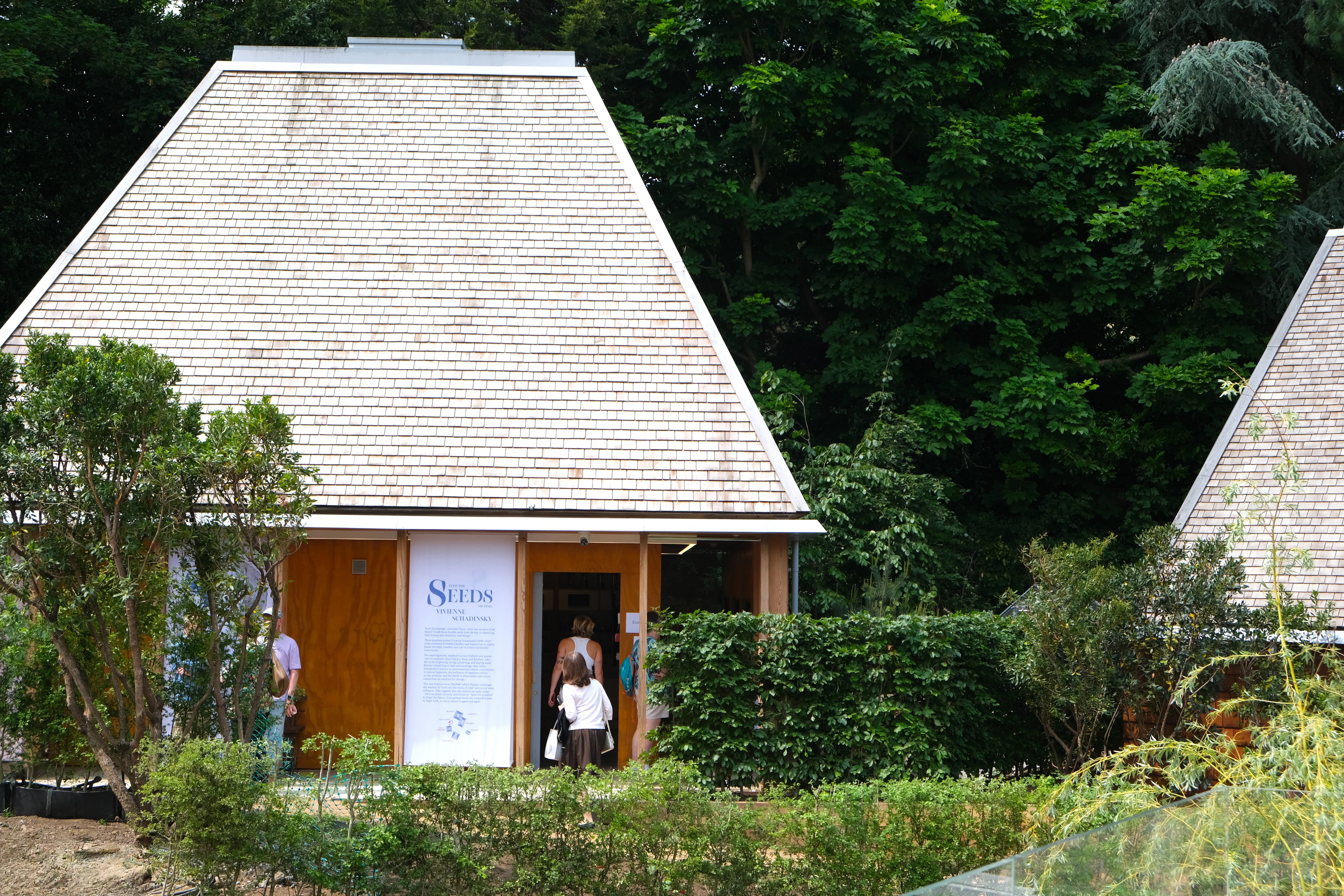Exterior view of Omved Gardens venue designed by Smerin Architects, showing the Douglas fir structure used for the Seed Vault event space. People are gathered outside during an event. Photo credit: Joanna Ayre