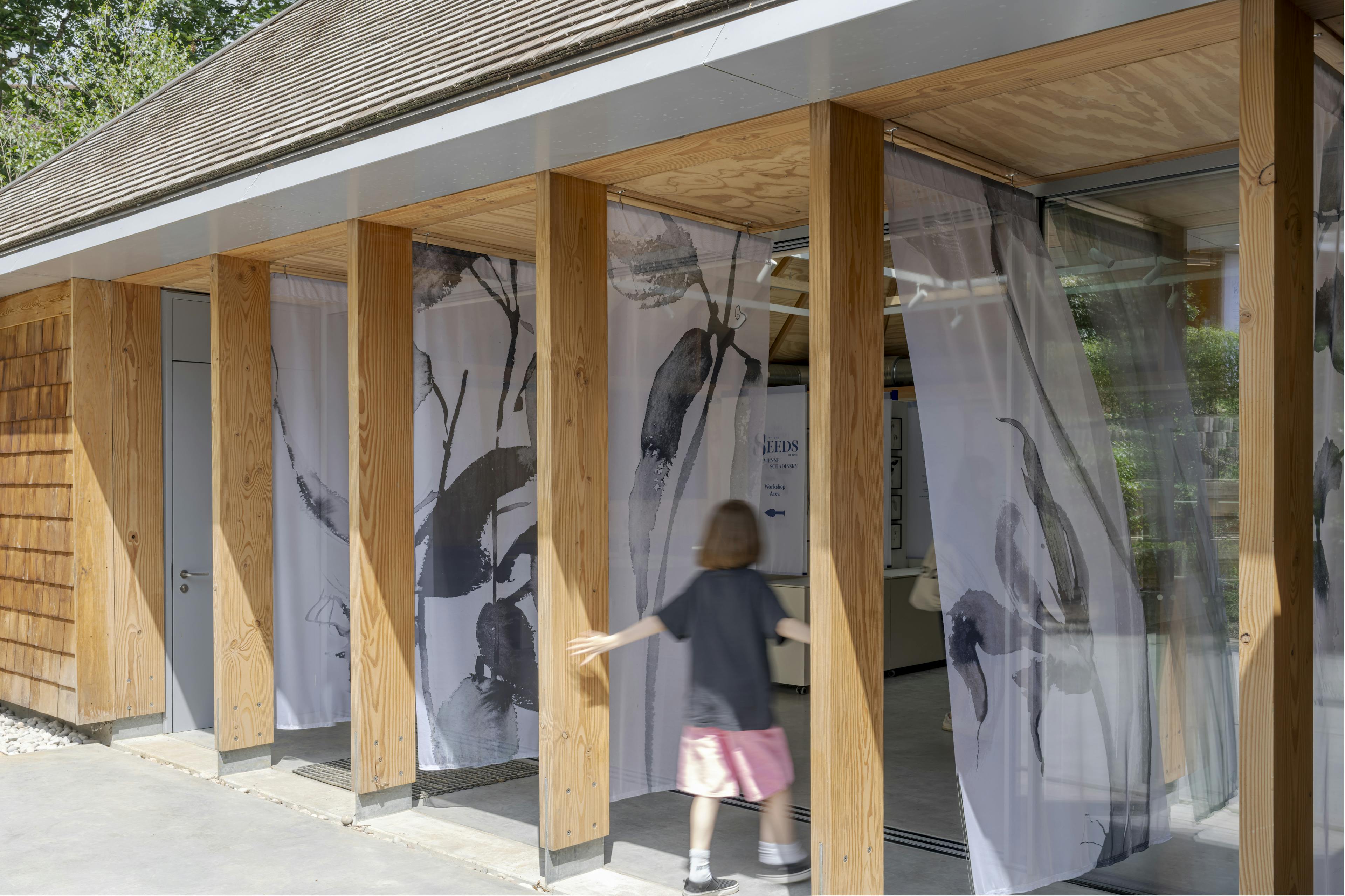 Exterior view of a Douglas fir-framed structure designed for events, with visible steel post feet anchoring the timber frame, set within a landscaped garden setting