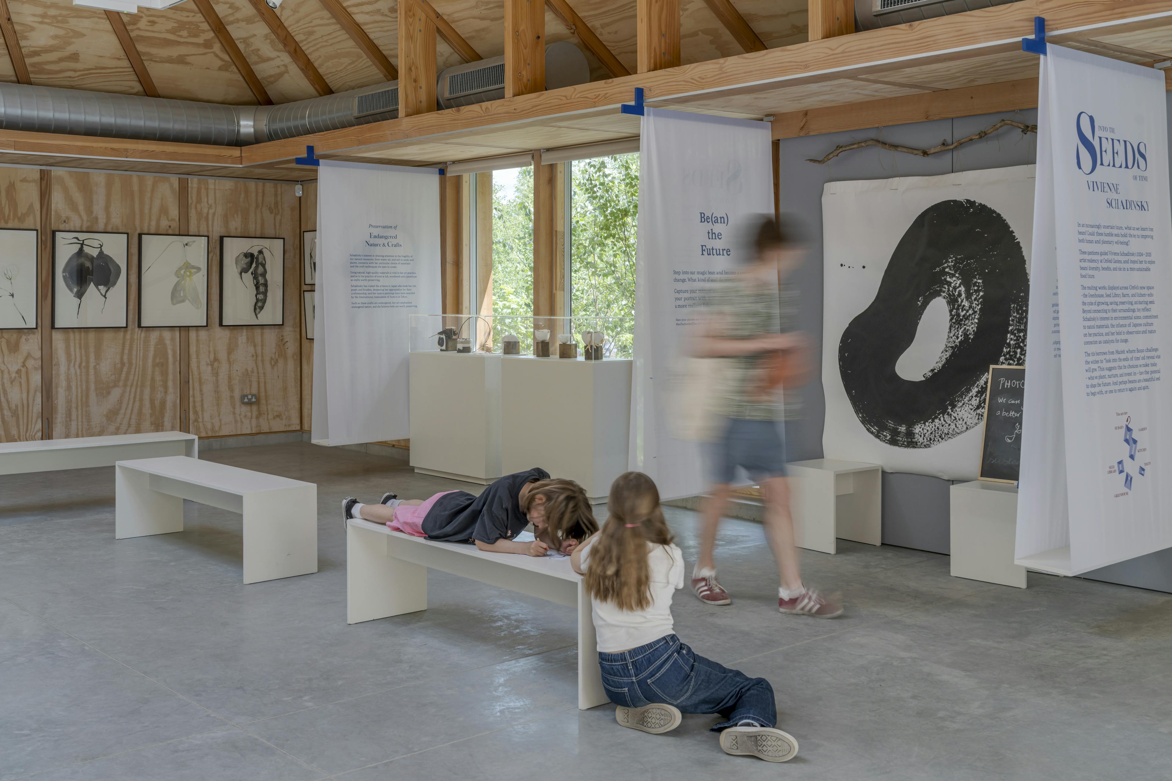Interior of a Douglas fir-framed event space with vaulted glazed ceiling and open-plan layout, where children are present during a seminar and exhibition