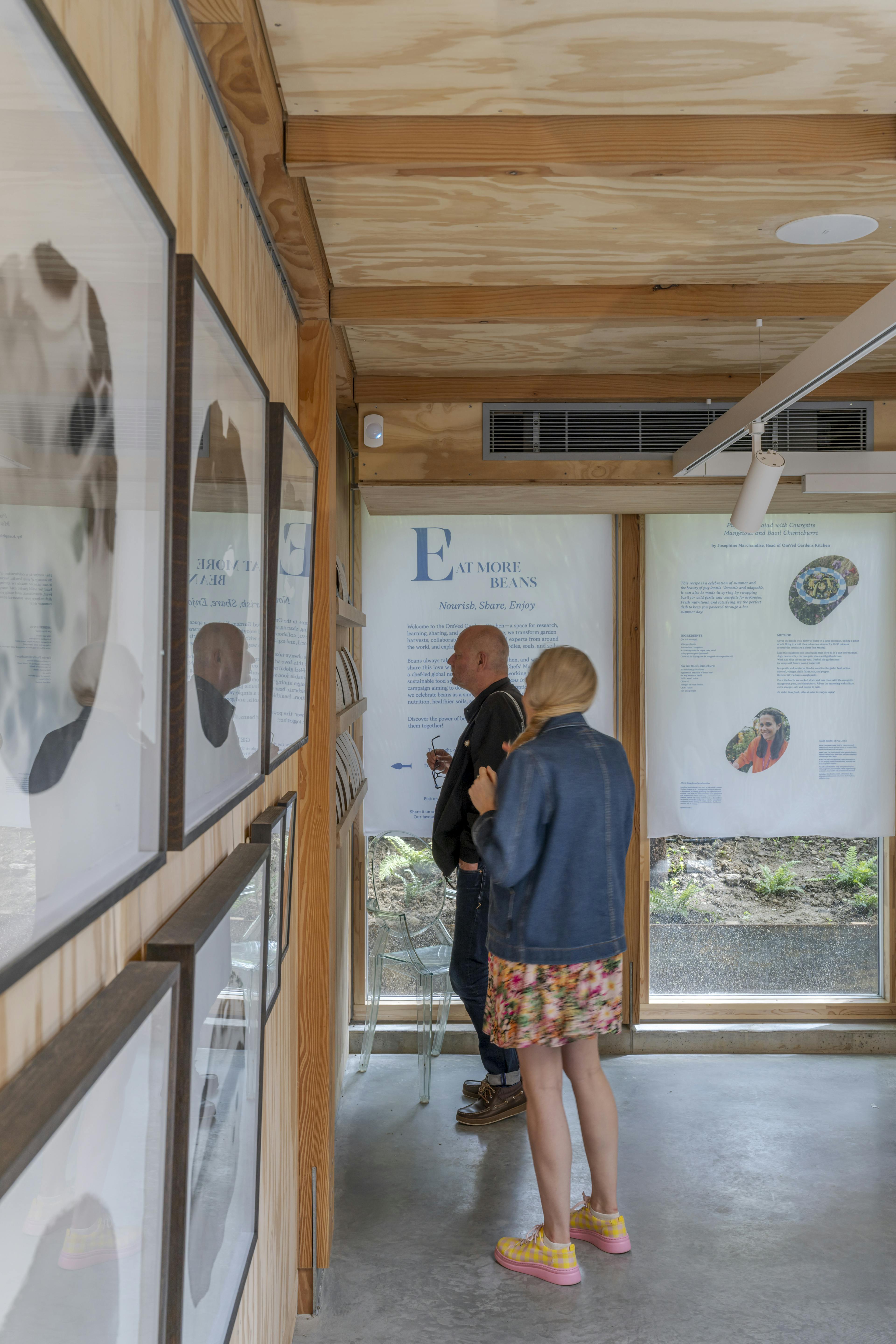 Interior of a Douglas fir-framed event space featuring a vaulted glazed ceiling and open-plan design, with members of the public attending a seminar and exhibition