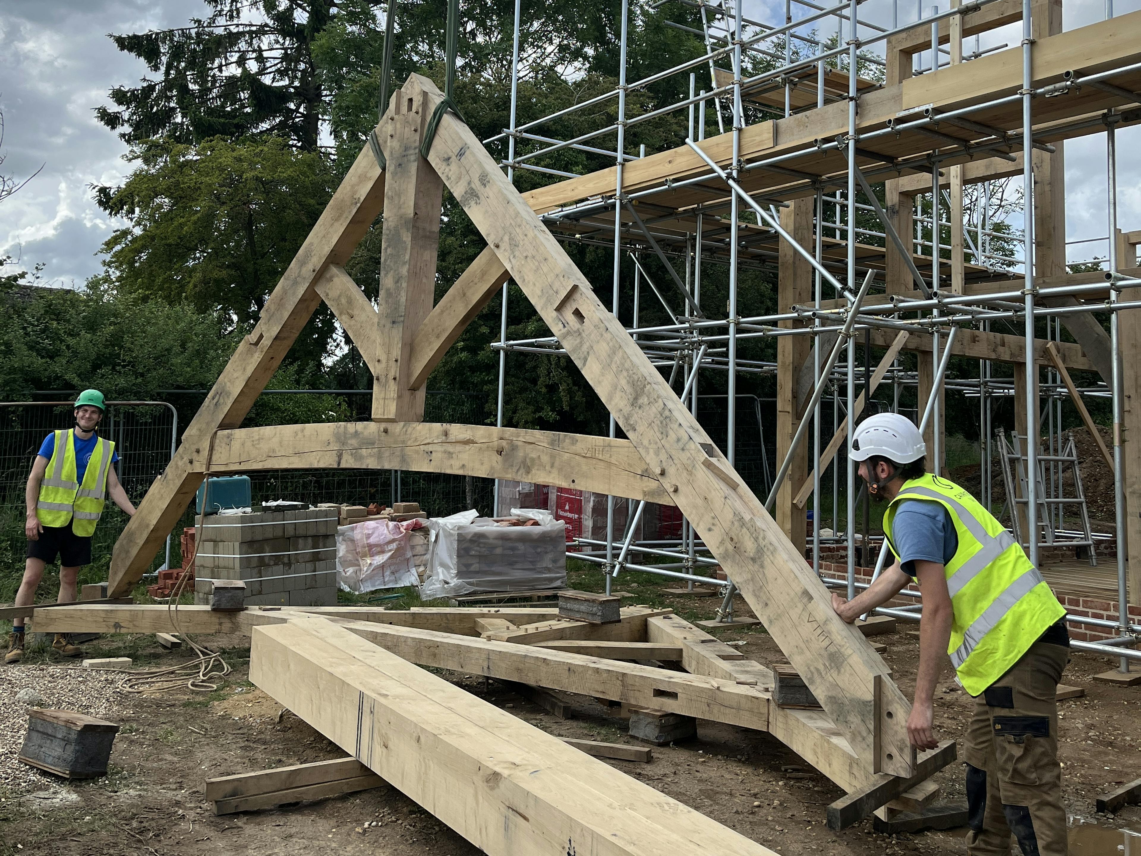 Carpenters steady a truss which is being lifted into place by a crane during construction of an oak frame home