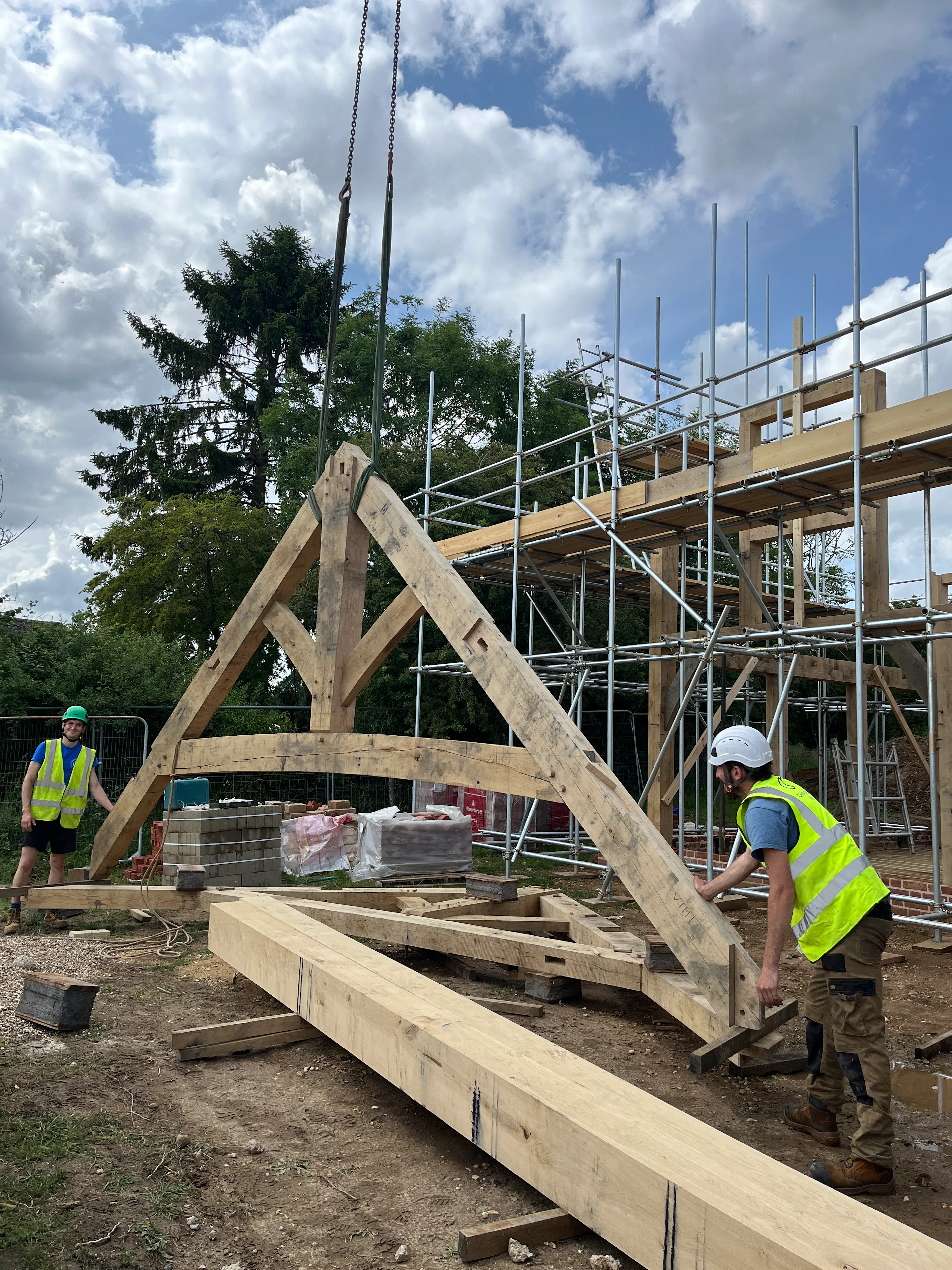 Carpenters steady a truss which is being lifted into place by a crane during construction of an oak frame home