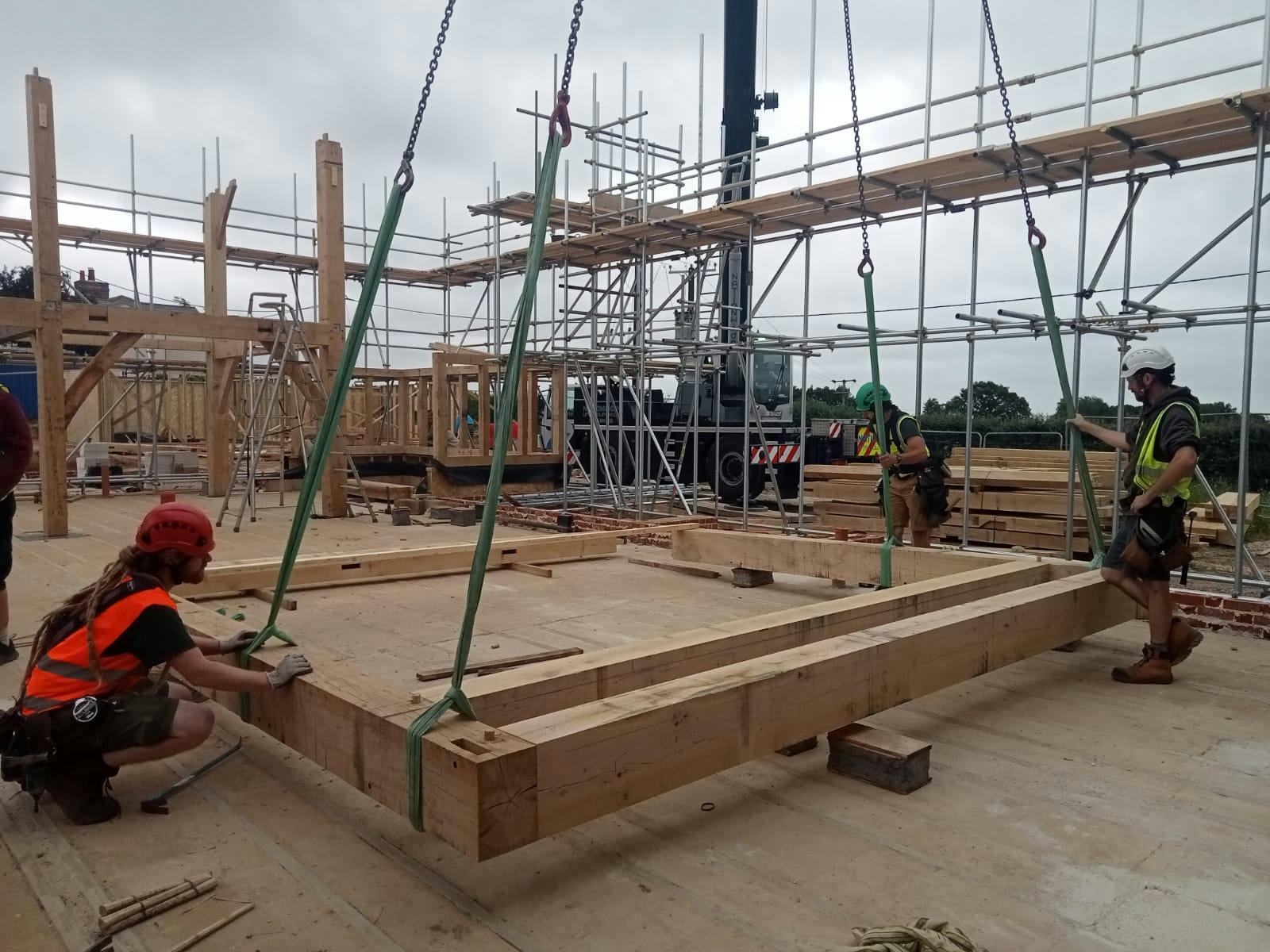 Carpenters with an oak frame being lifted into place by a crane during construction of an oak frame home