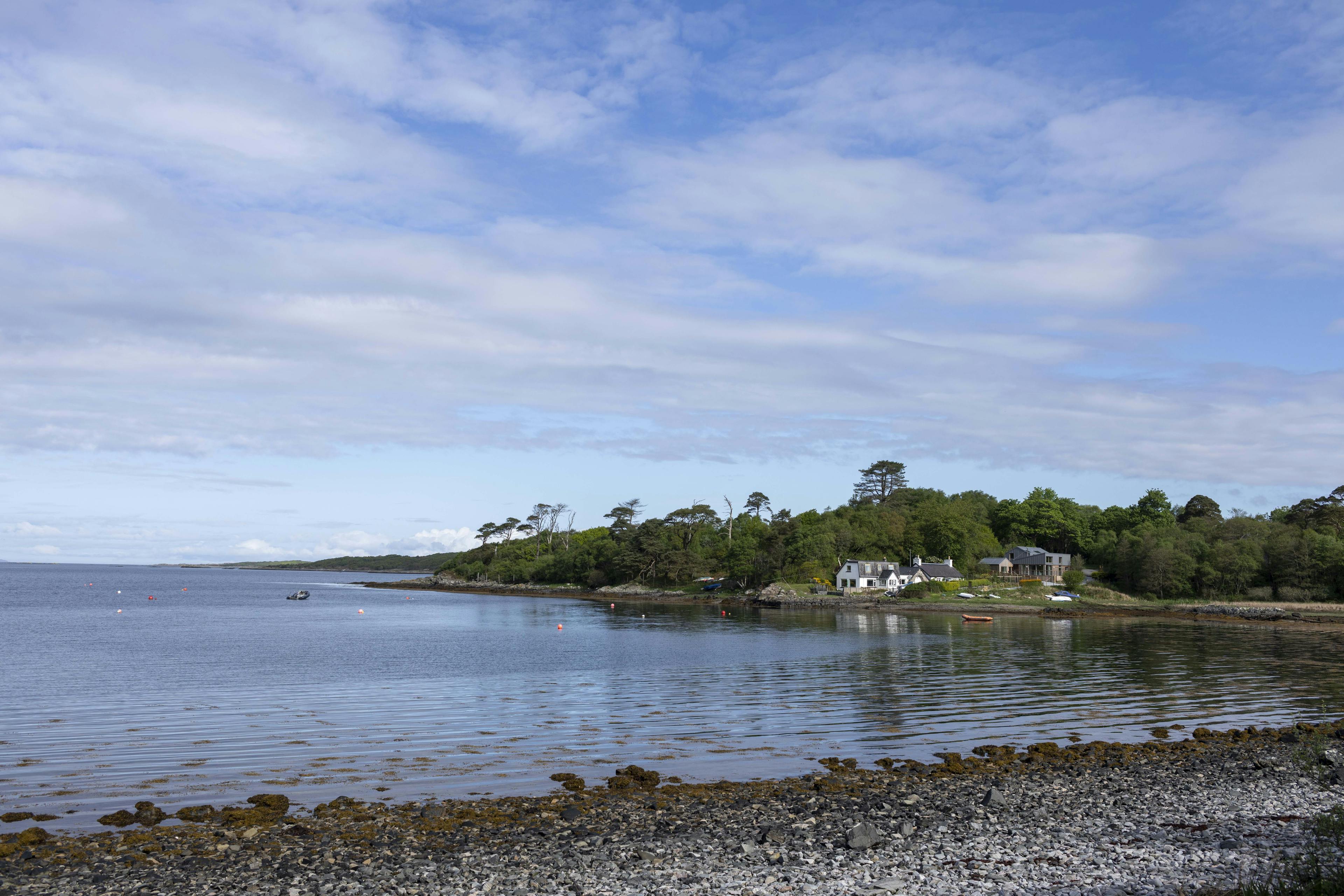 A shoreline in the Scottish Highlands west coast with some old cottages and a newly built home in the distance on the shoreline