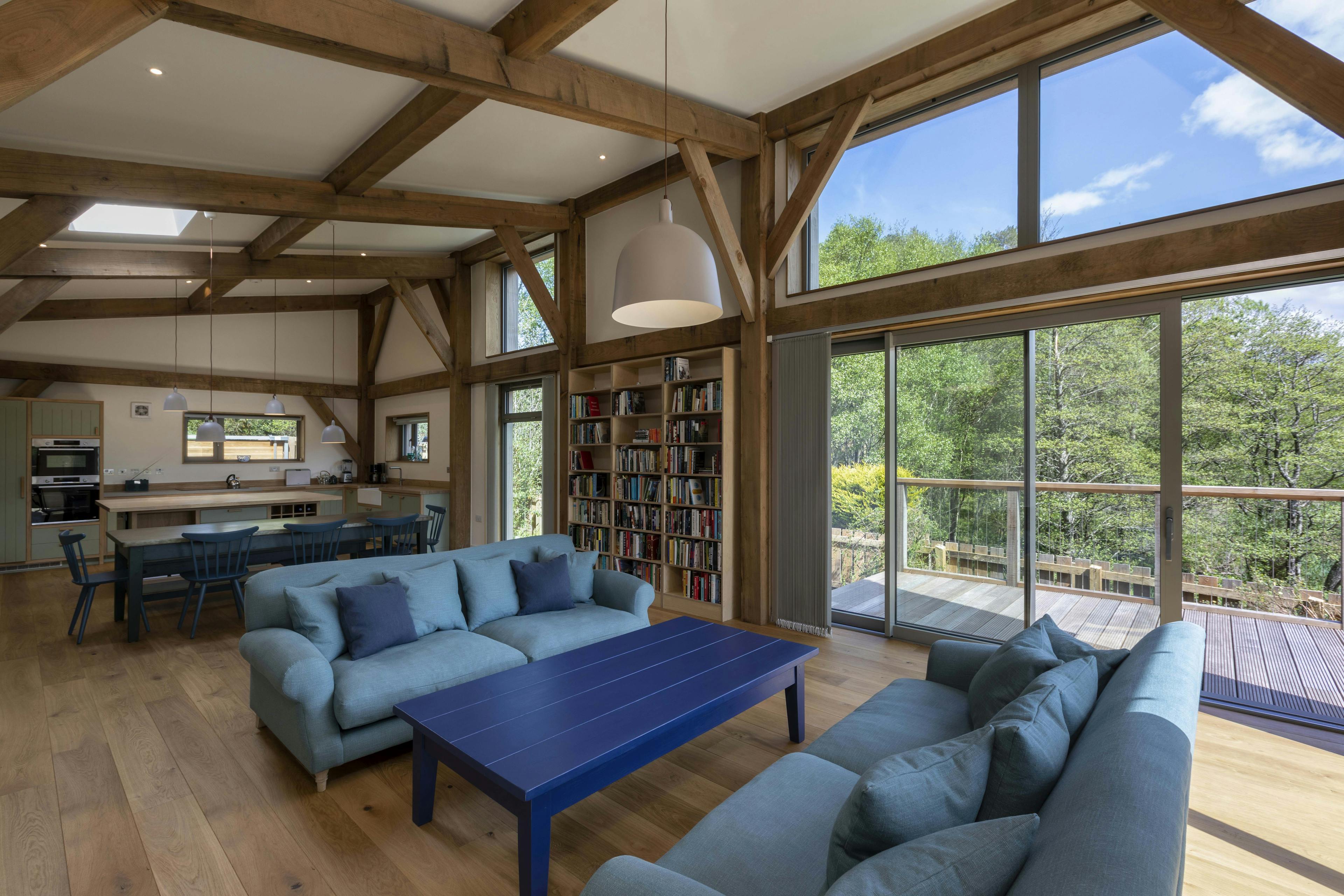 A living area with sofas, dining area and kitchen under a Douglas fir framed mono pitched roof