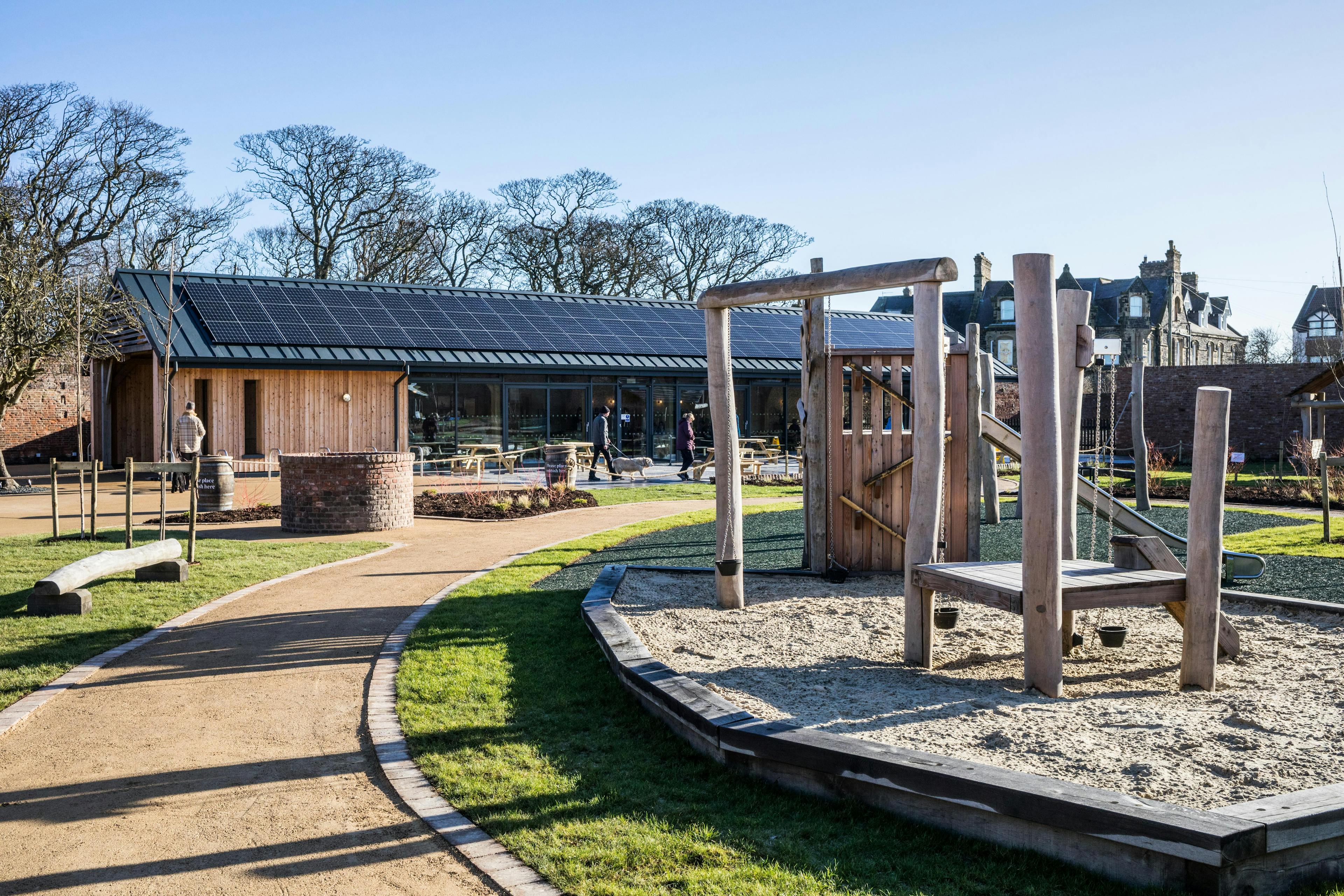 The garden of an oak framed cafe with solar panels on the roof and a children's play area in the foreground