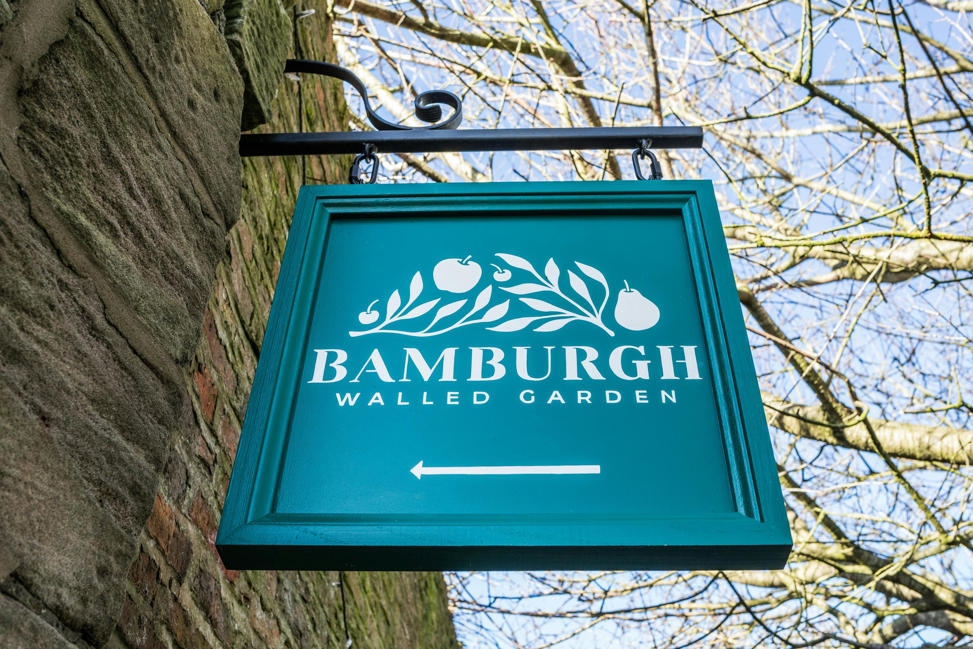 A green sign for a walled garden cafe, hanging from a stone wall.