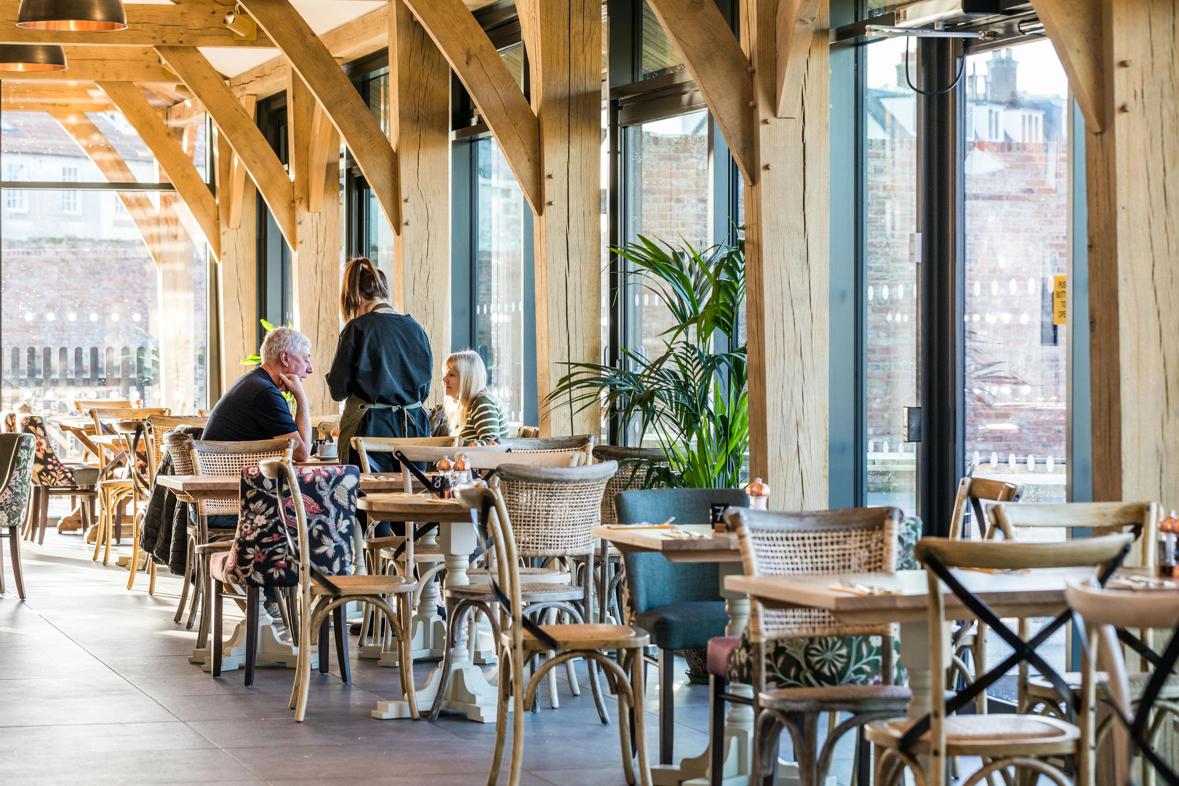 Internal image of an oak framed cafe with customers at a table and a waitress