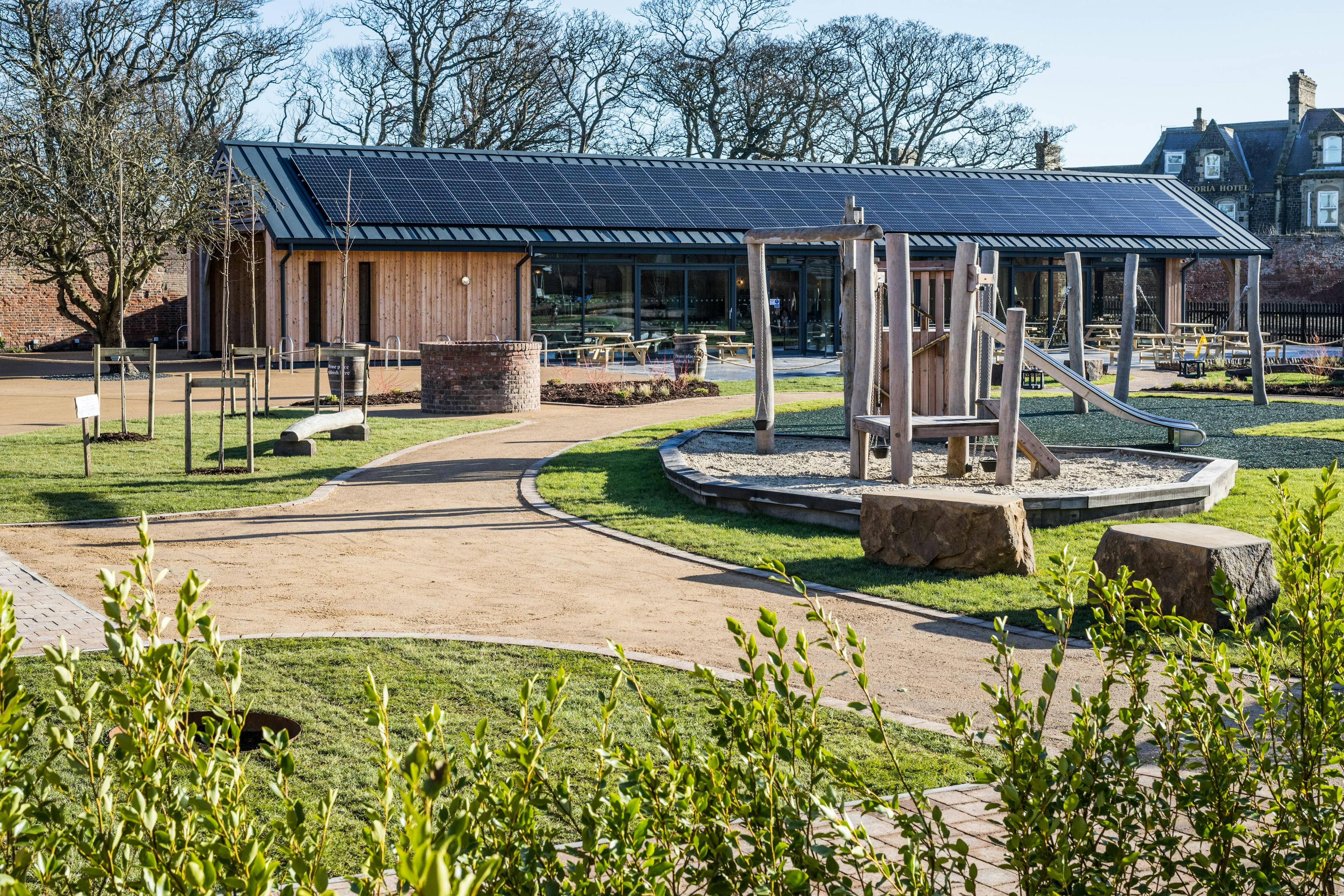 The garden of an oak framed cafe with solar panels on the roof and a children's play area in the foreground