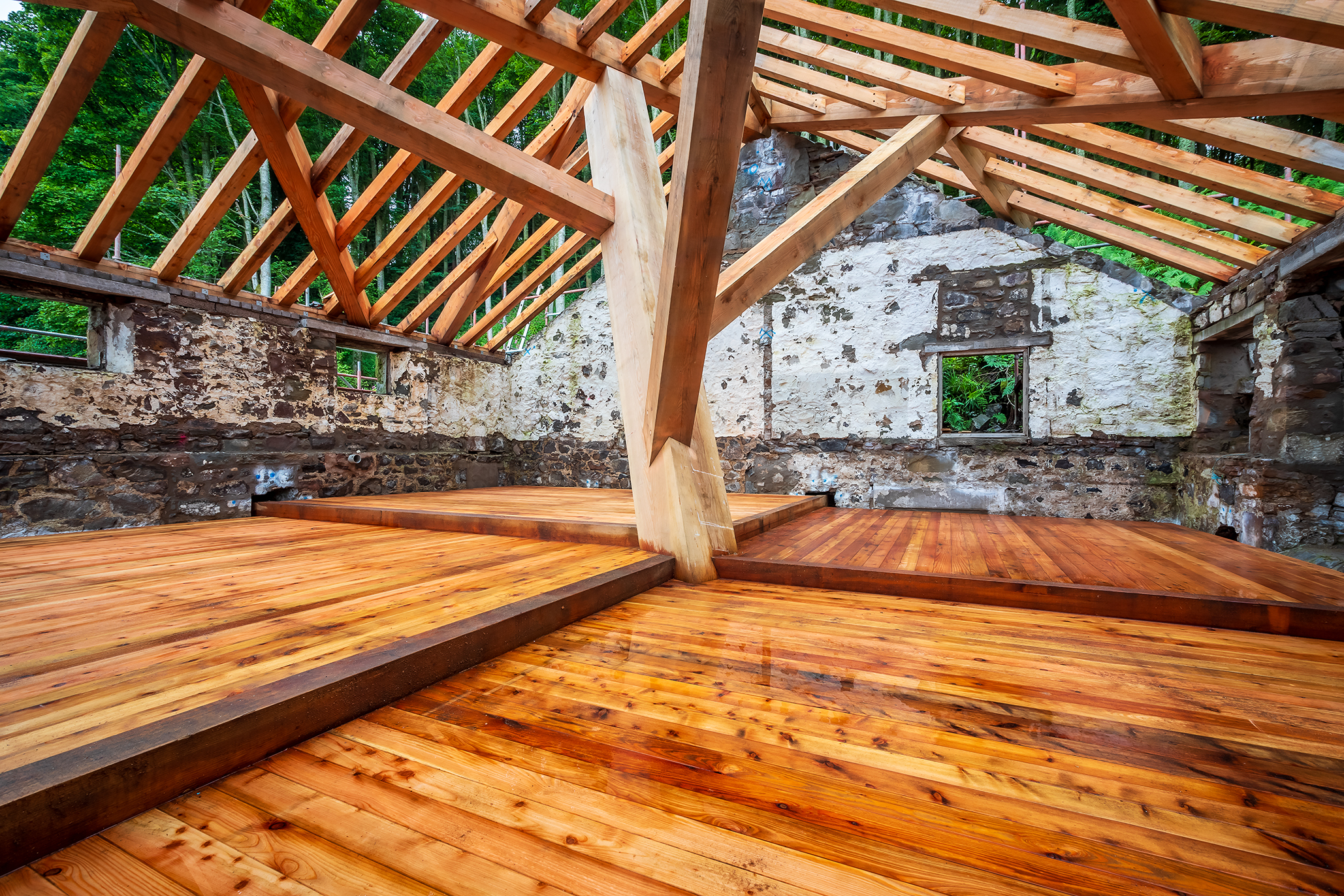A complex structural timber frame and wooden flooring installed in a boathouse on the shore of a river