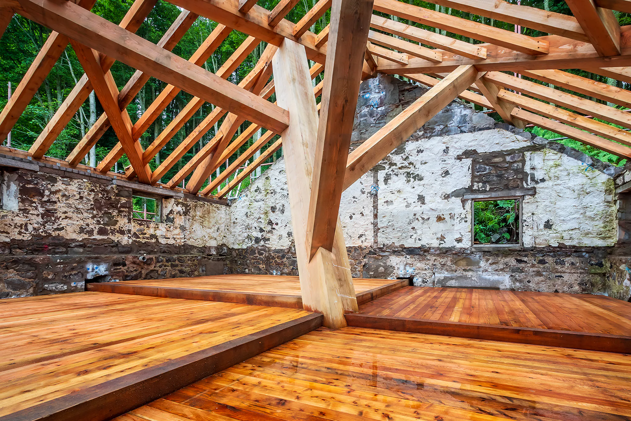 A complex structural timber frame and wooden flooring installed in a boathouse on the shore of a river