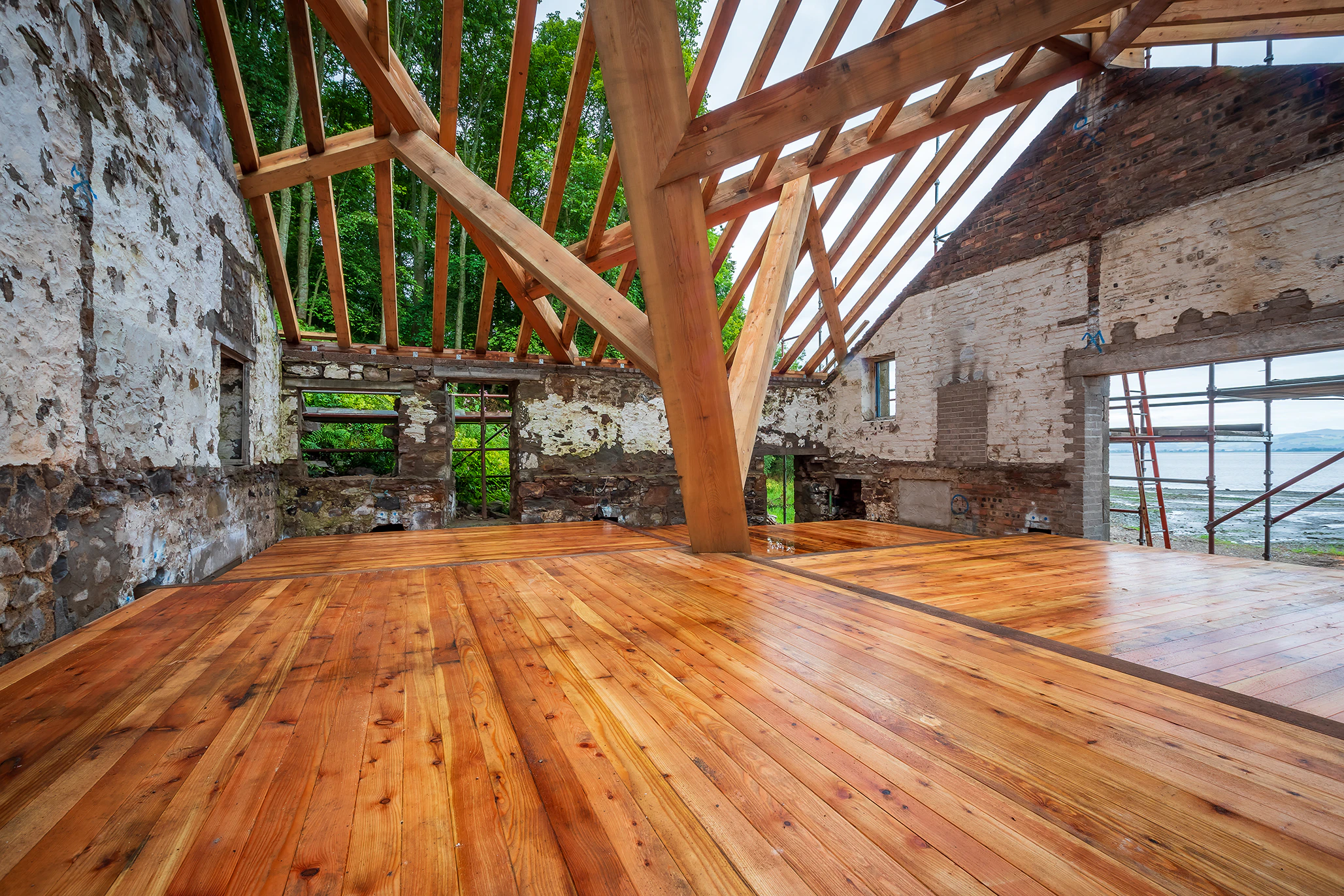 A complex structural timber frame and wooden flooring installed in a boathouse on the shore of a river