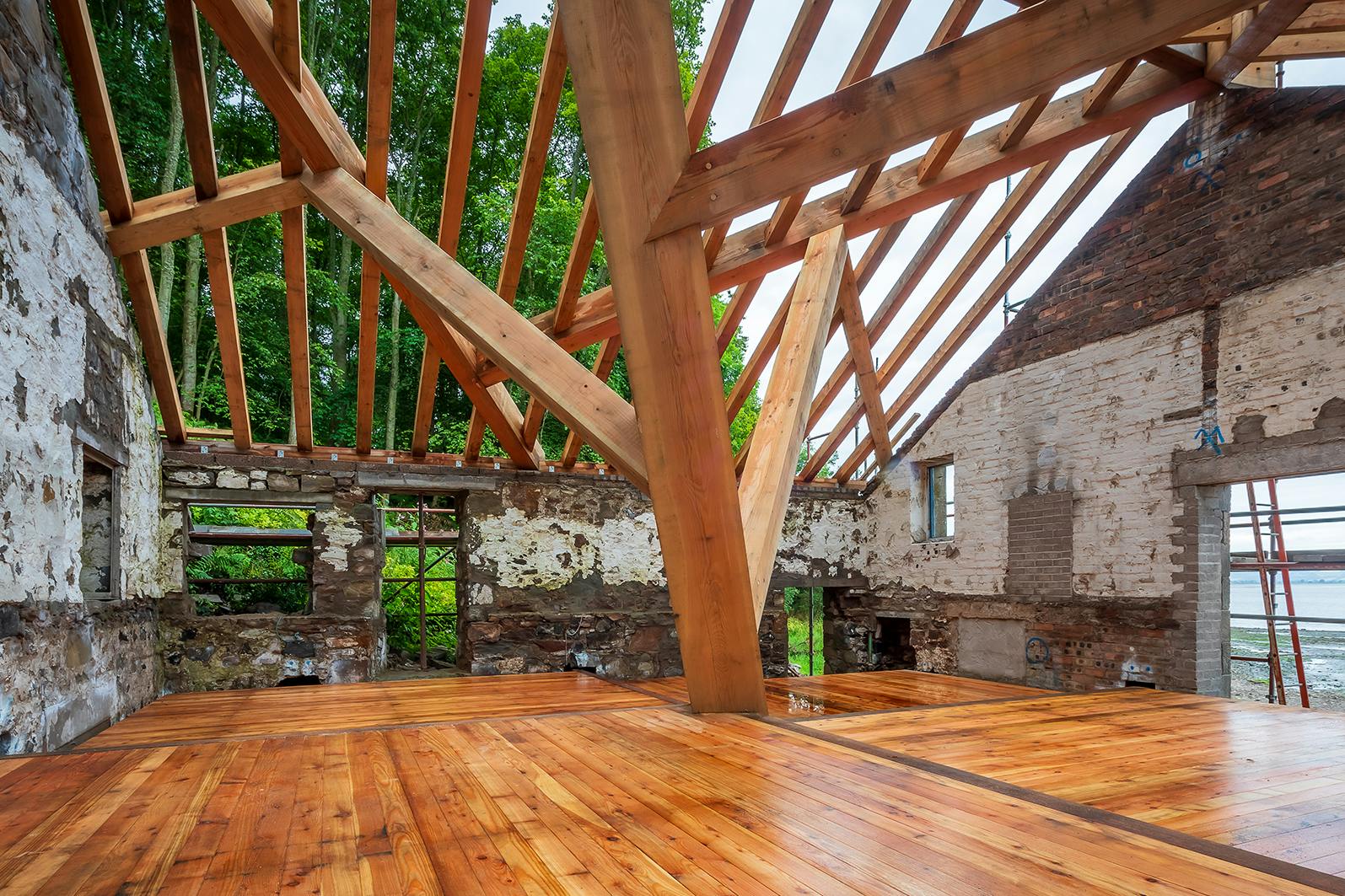 A complex structural timber frame and wooden flooring installed in a boathouse on the shore of a river