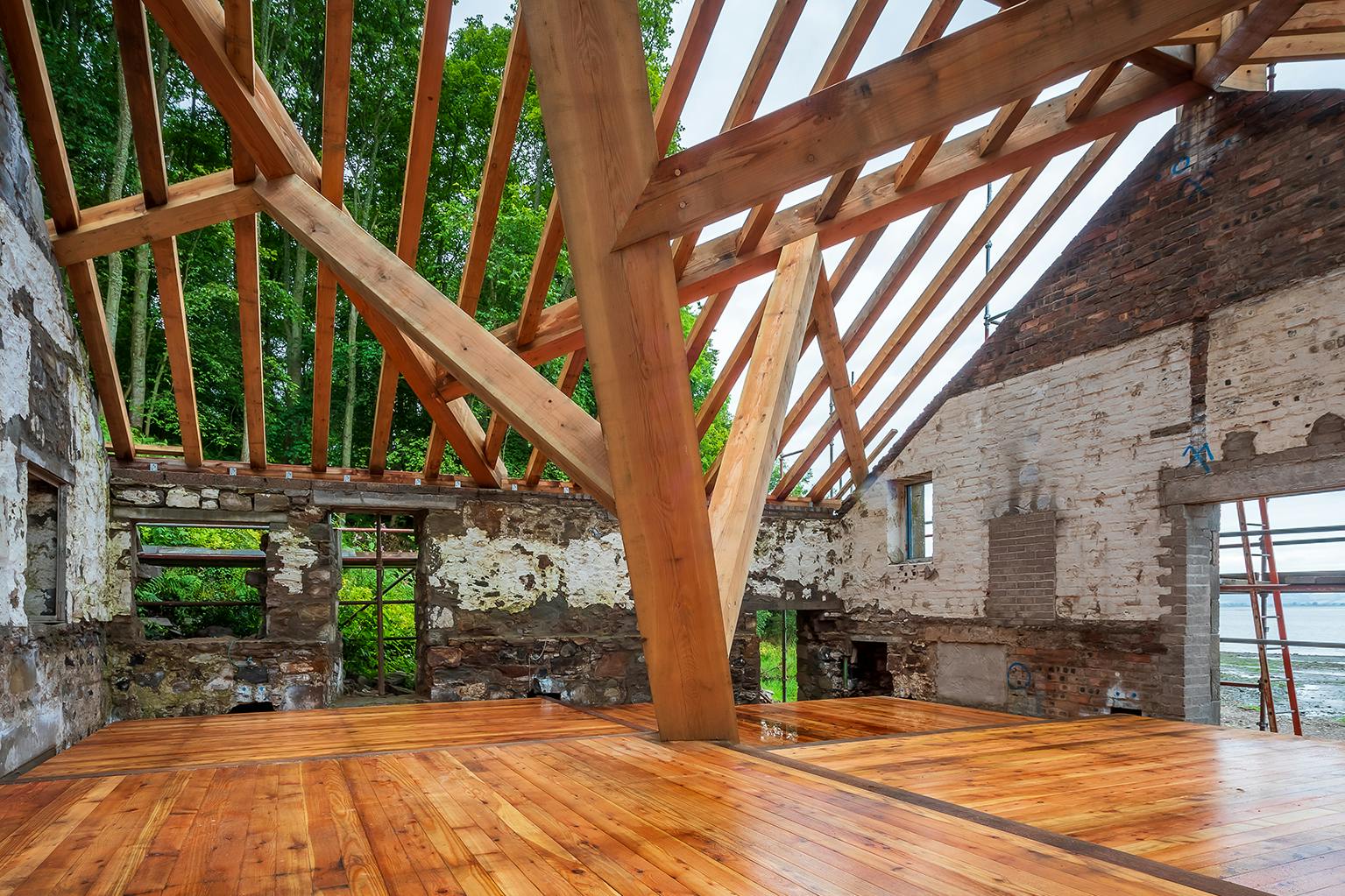 A complex structural timber frame and wooden flooring installed in a boathouse on the shore of a river
